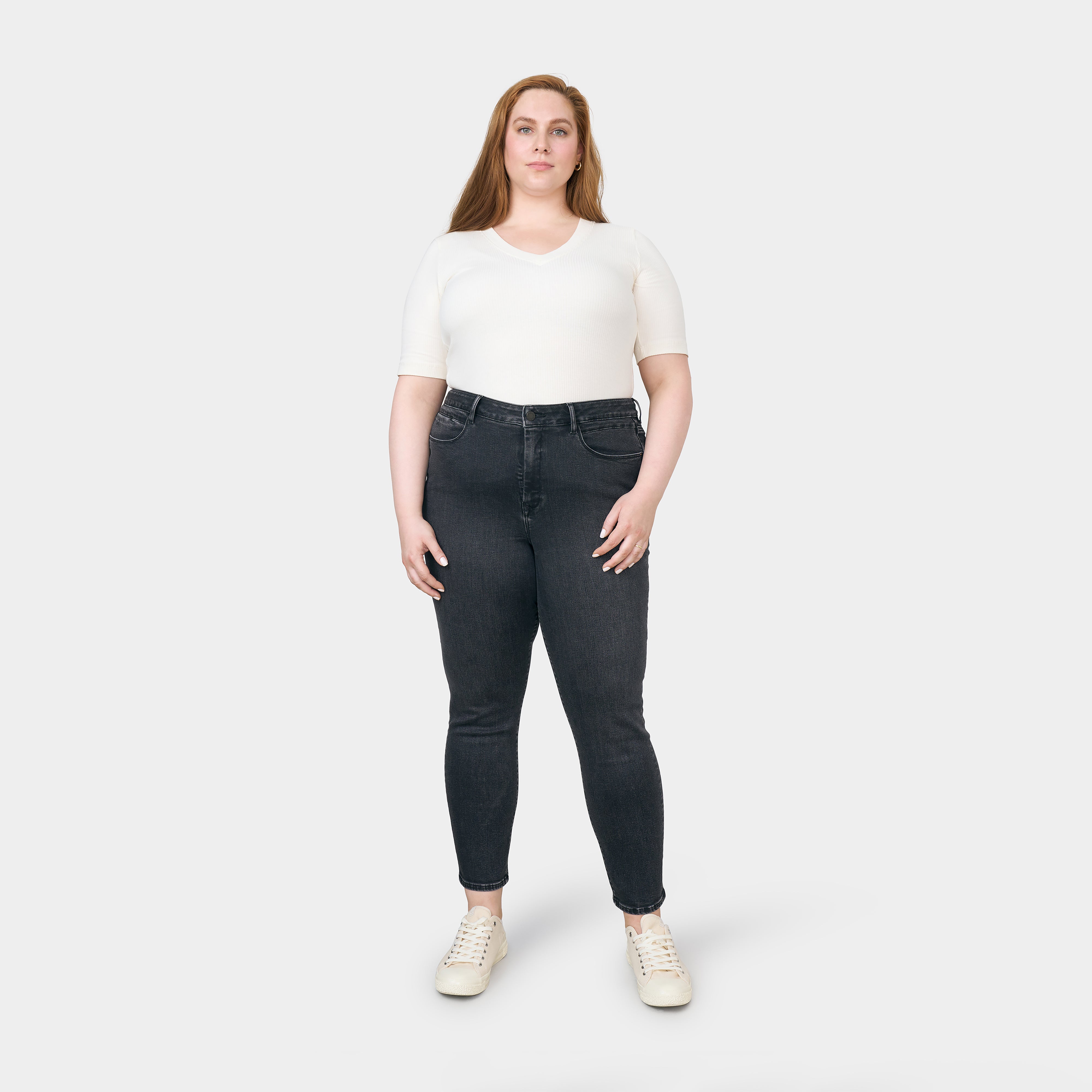SUN UP Skinny Jeans Curvy in Black Denim mit Powerstretch, mittelhoher Sitz, minimalistische Details an den Vordertaschen; getragen von einer Frau in weißem Top und Sneakers.