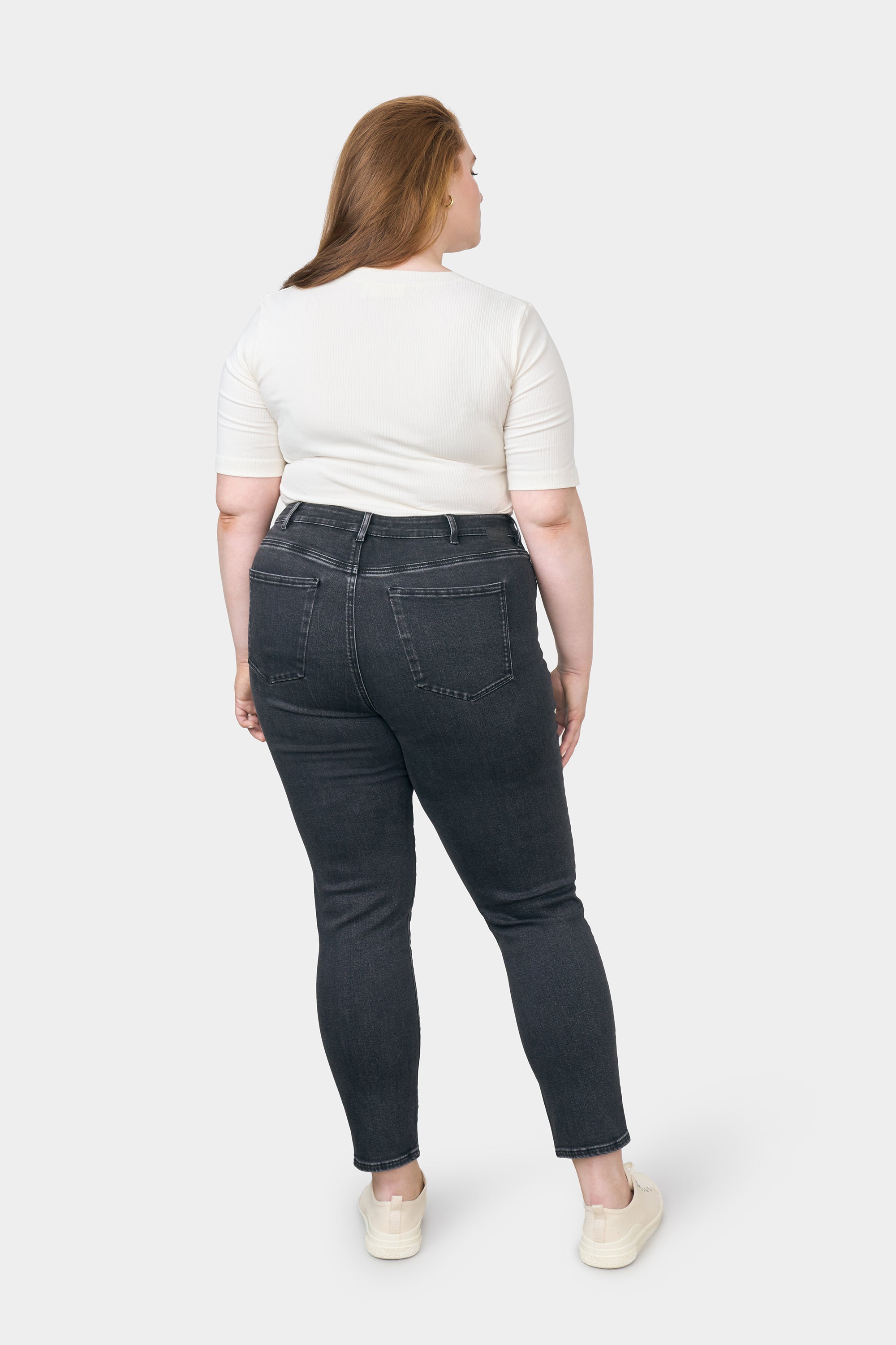 Rückansicht einer kurvigen Frau in SUN UP Skinny Powerstretch Black Denim; dunkelblaue Jeans mit zwei Gesäßtaschen, weißes Oberteil.