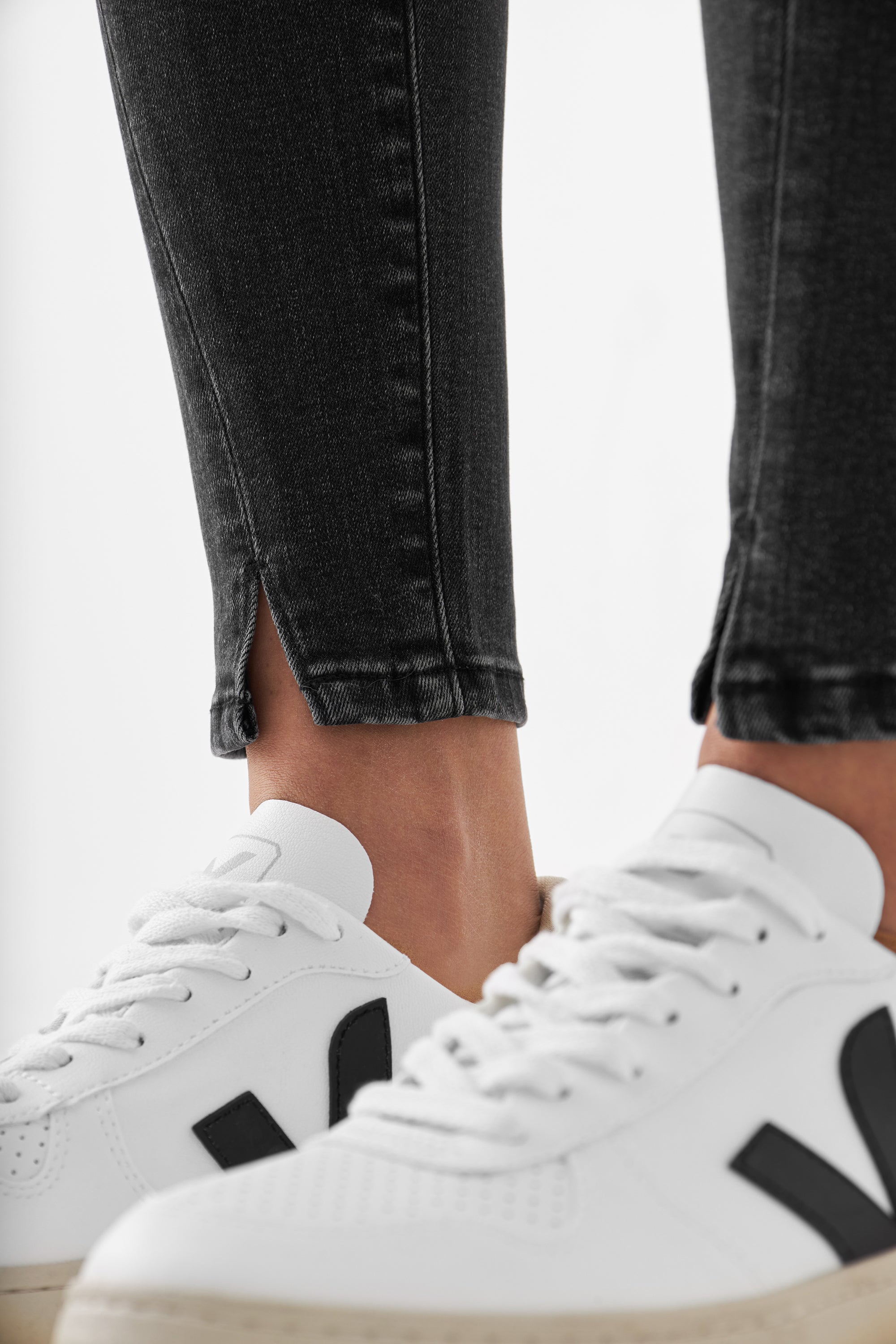 SUN UP Skinny Jeans in Black Denim mit Saumschlitz; enge Passform, Beinpartie eines Models in weißen Sneakern.
