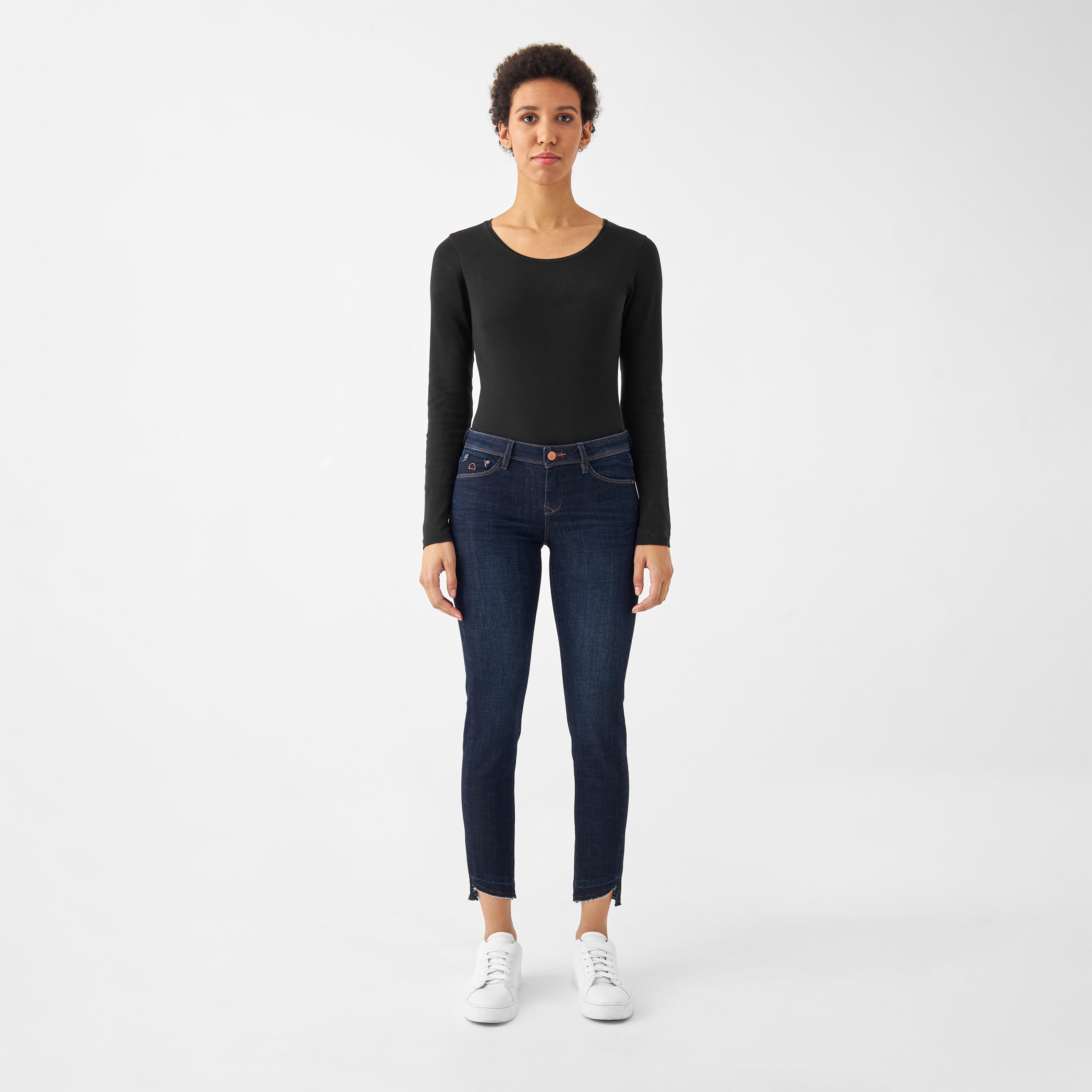 Frontansicht: dunkle MID SUN Slim-Fit Jeans mit offenem, fransigem Saum und klassischem 5-Pocket-Design, getragen zu schwarzem Oberteil und weißen Sneakern.