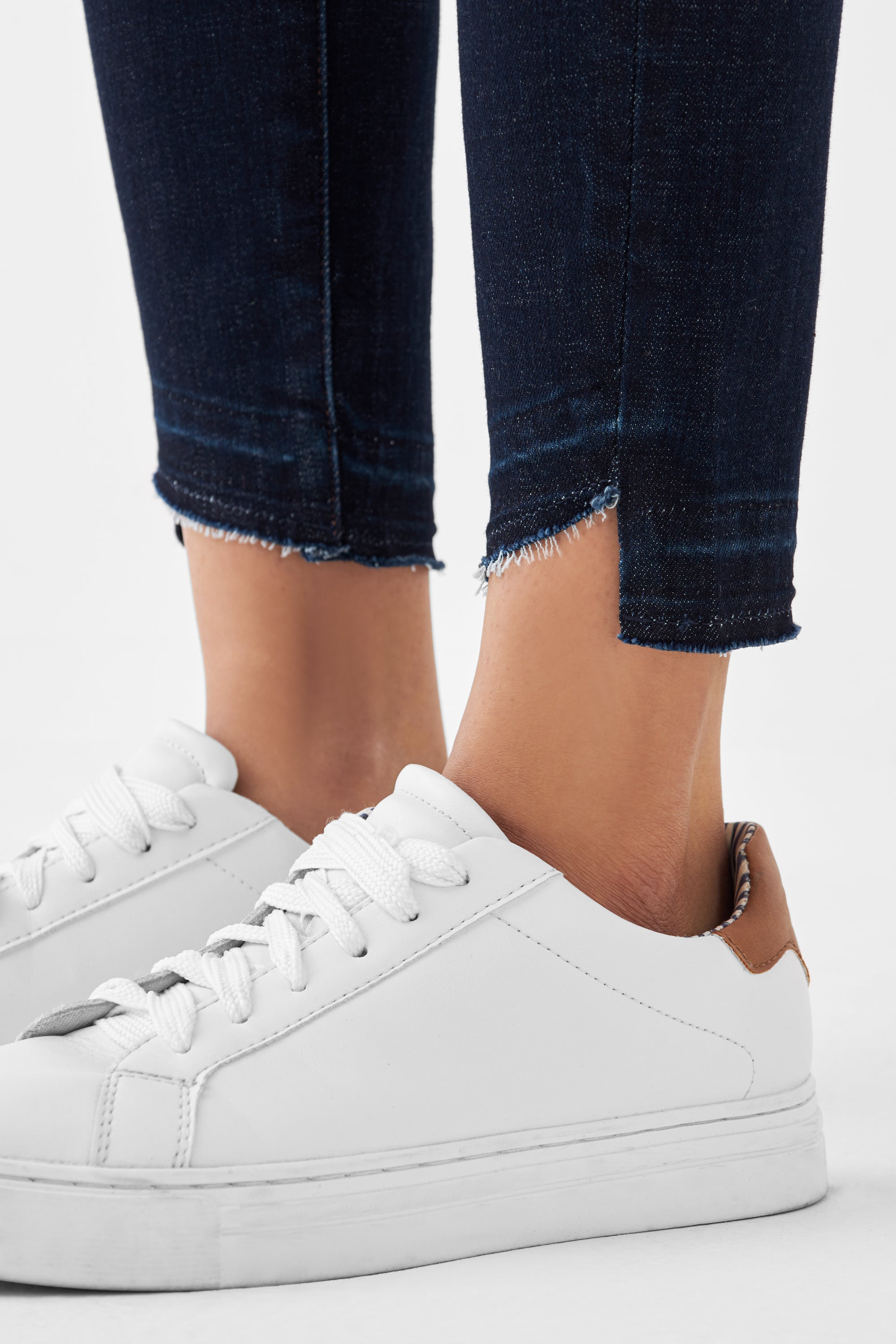 Dunkelblaue MID SUN Slim Comfortstretch Jeans mit offenem, fransigem Saum am Knöchel, kombiniert mit weißen Sneakern.