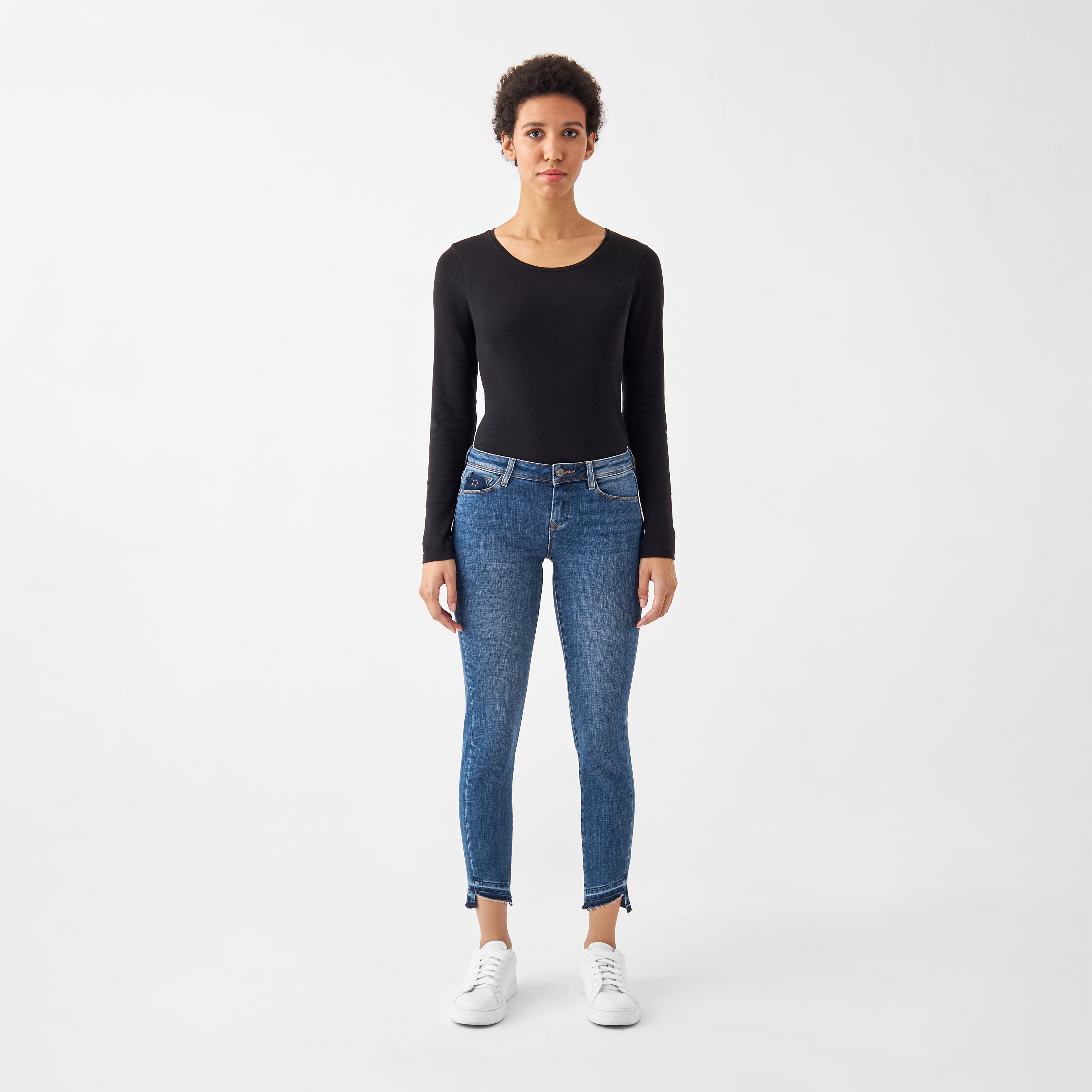 Model trägt MID SUN Slim Comfortstretch Jeans in Medium Blue – Slim-Fit, niedrige Taille, 5-Pocket-Design, offener, fransiger Saum; Bio-Baumwolle.