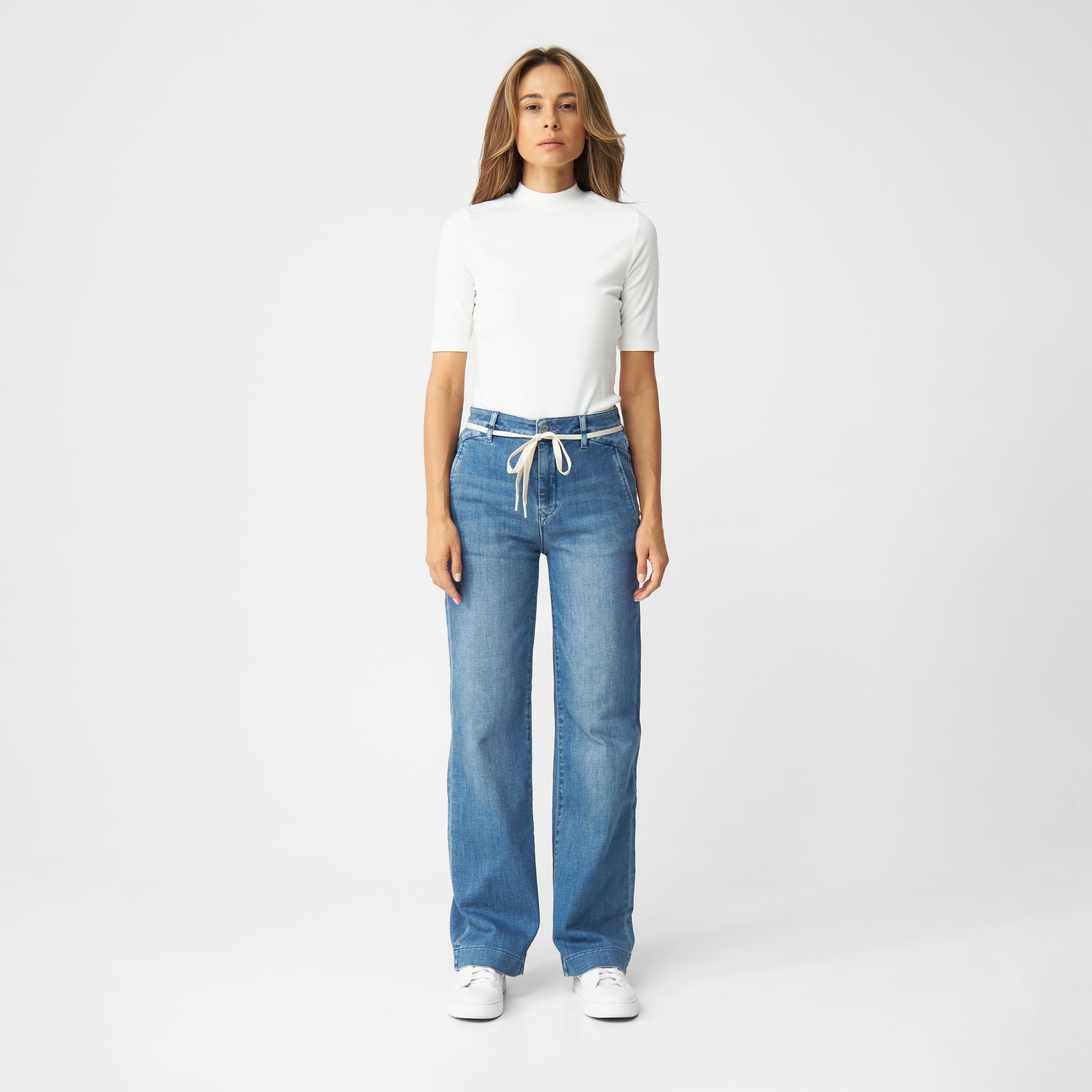 DEW Flared Soft Denim in Medium Blue: High-Waist Jeans mit ausgestelltem Bein, französische Taschen; hellbeigefarbener Gürtel.