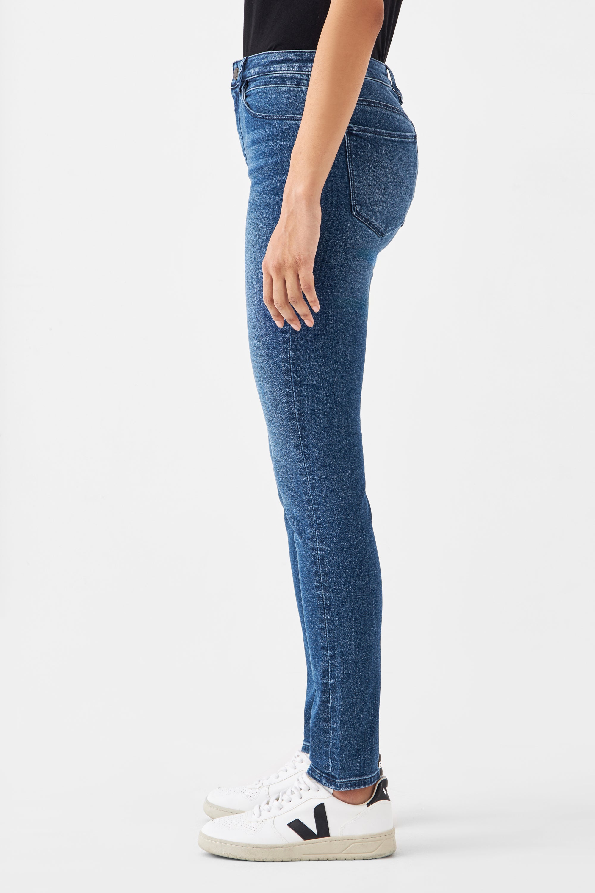 Seitliche Ansicht einer Person in SUN UP Basic Skinny Jeans in Medium Blue; eng sitzende Powerstretch-Jeans mit minimalistischen Vordertaschen-Details, dazu weiße Sneaker.