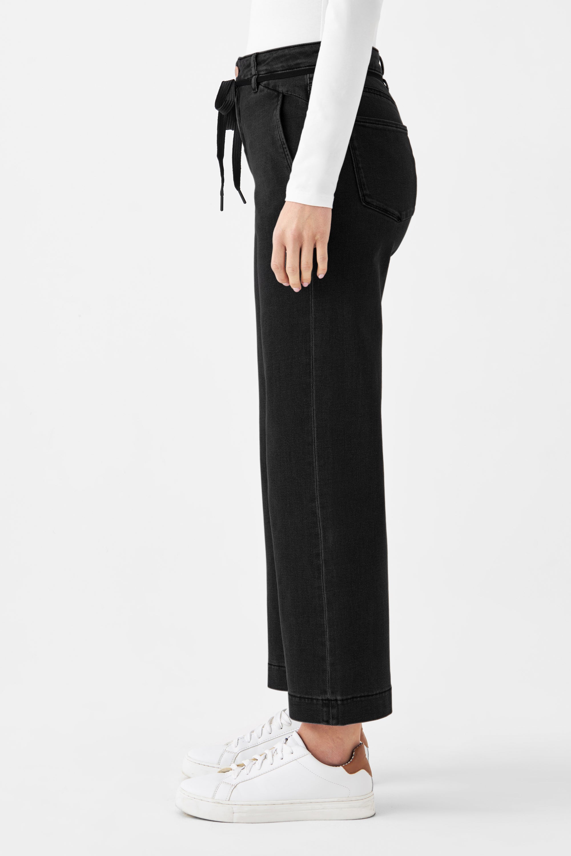Seitenansicht der schwarzen DEW Cropped Flared Jeans mit hohem Bund, ausgestelltem Bein und französischen Taschen; Bindegürtel am Bund.