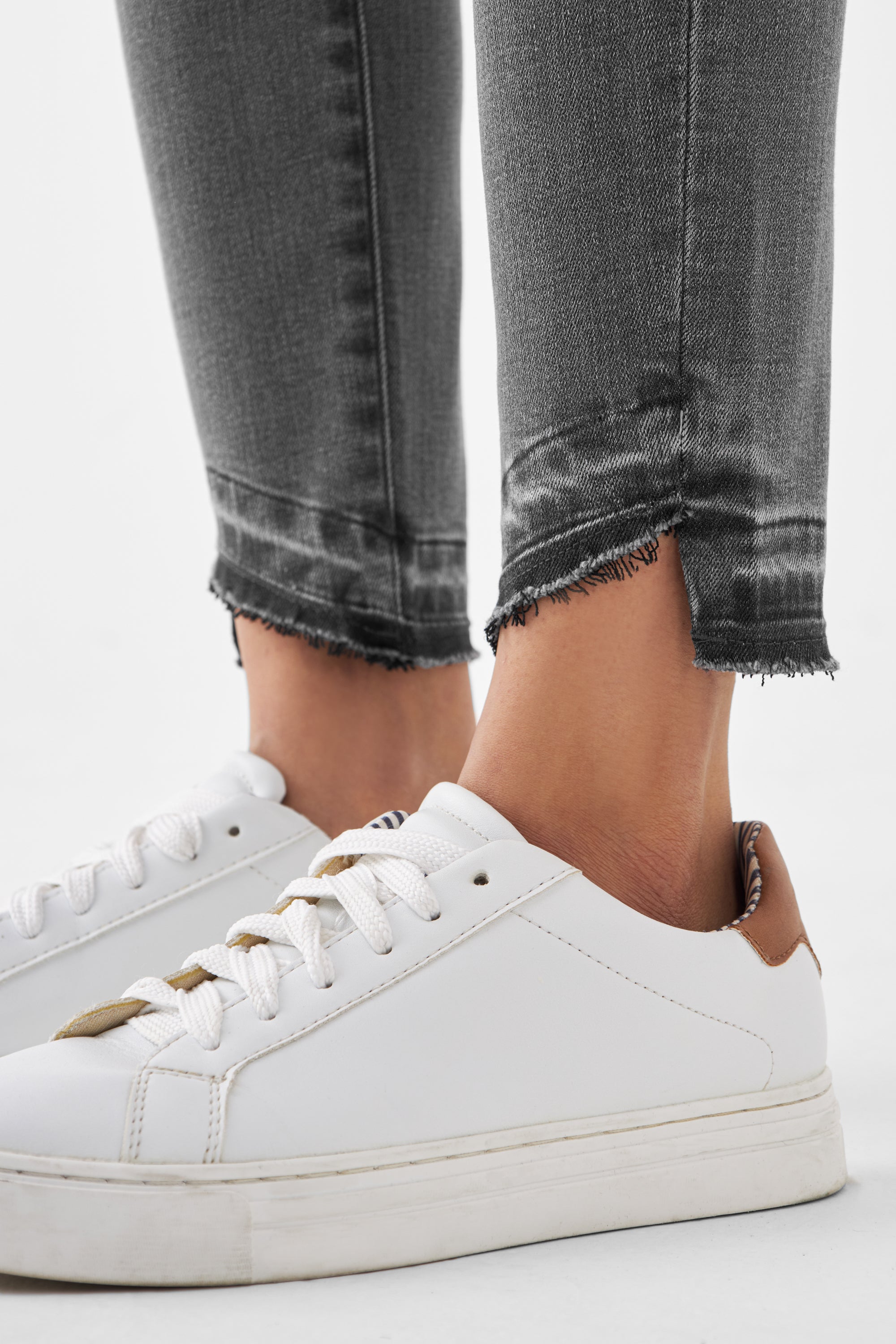 Dunkelgraue MID SUN Slim-Fit Jeans aus Organic Comfortstretch mit offenem, fransigem Saum am Beinabschluss, kombiniert mit weißen Sneakern.