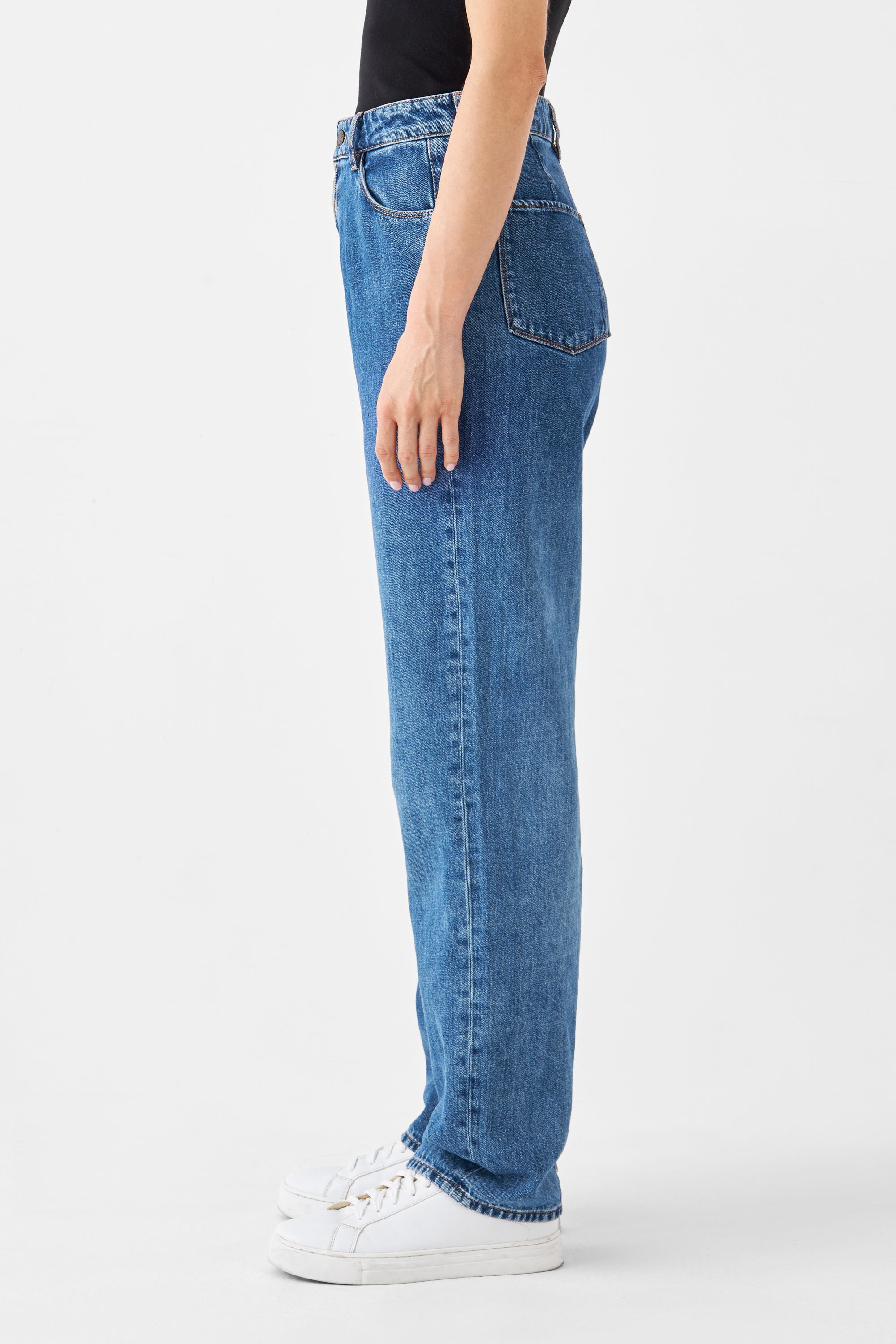 Seitenansicht einer Person in DAWN High-Waist Wide-Straight Jeans aus Bio-Baumwolle und Hanf, mittleres Blau, nicht dehnbar, mit weißen Sneakern.
