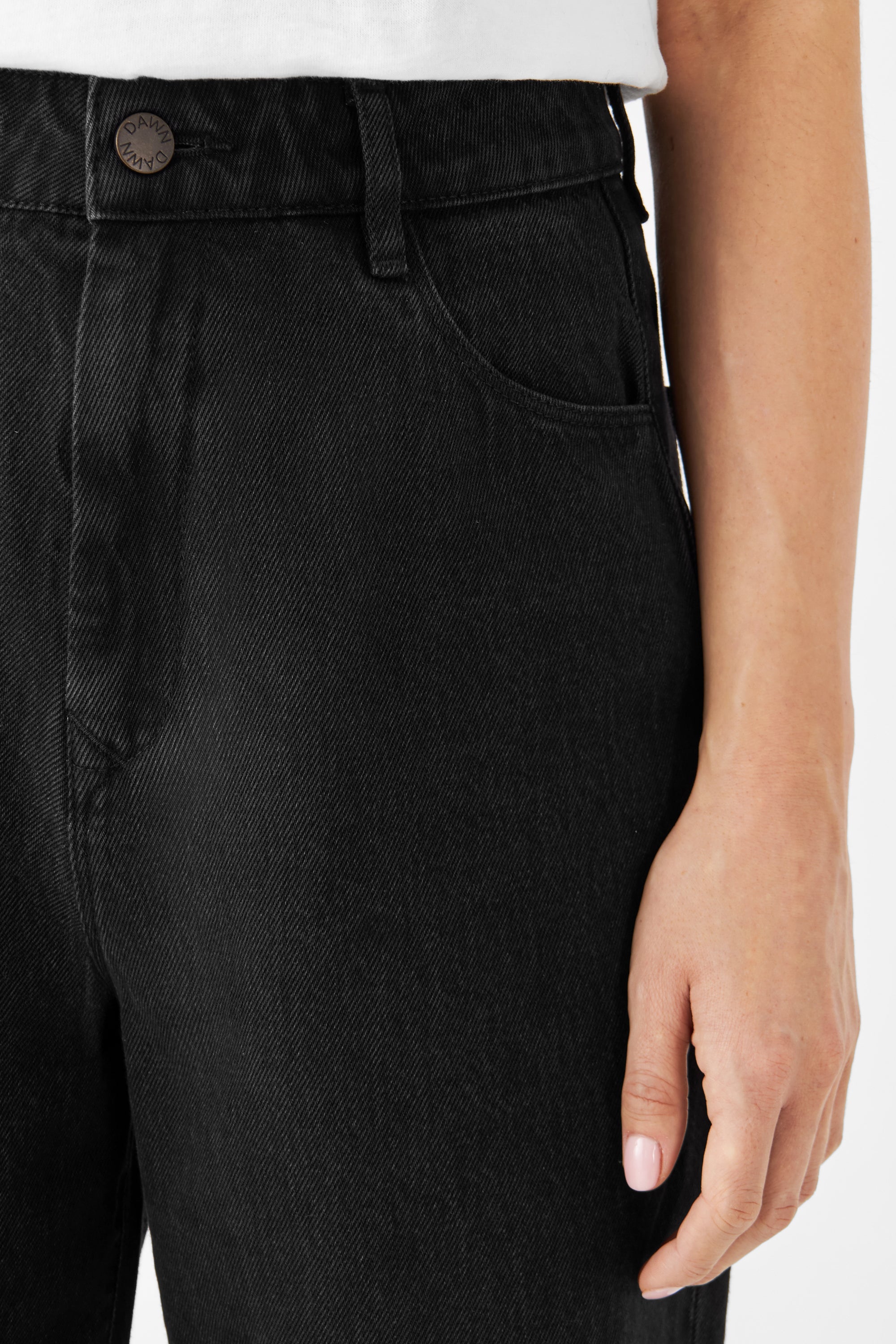 Nahaufnahme einer schwarzen DAWN Denim-Jeans in High-Waist mit geradem Schnitt; Fronttasche, Gürtelloop, DAWN-Metallknopf – Bio-Baumwolle.