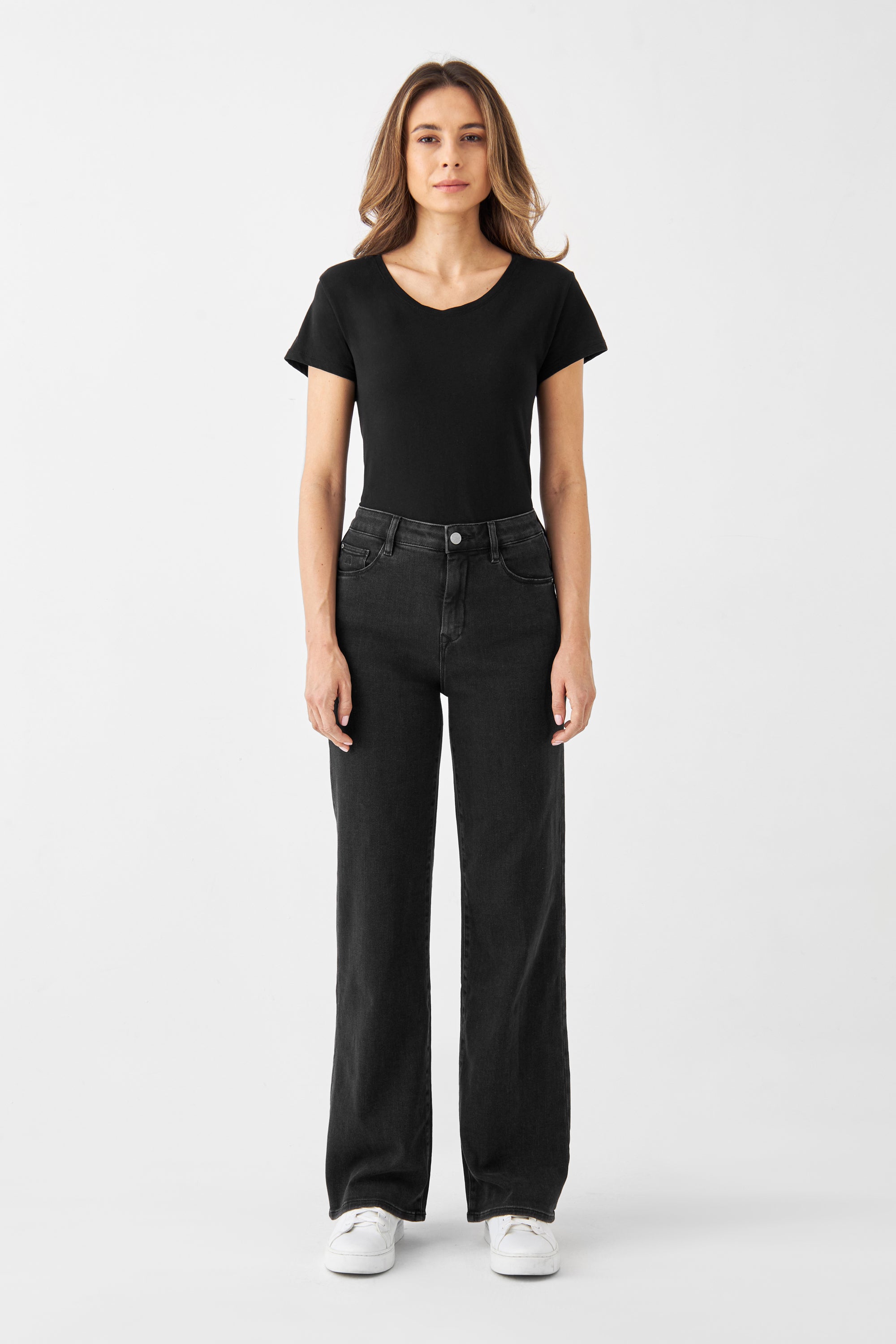 Modell trägt DEW Classic Black Denim: hohe Taille, ausgestelltes Bein (Flare), Five-Pocket-Design aus Organic Soft Denim mit Stretch.