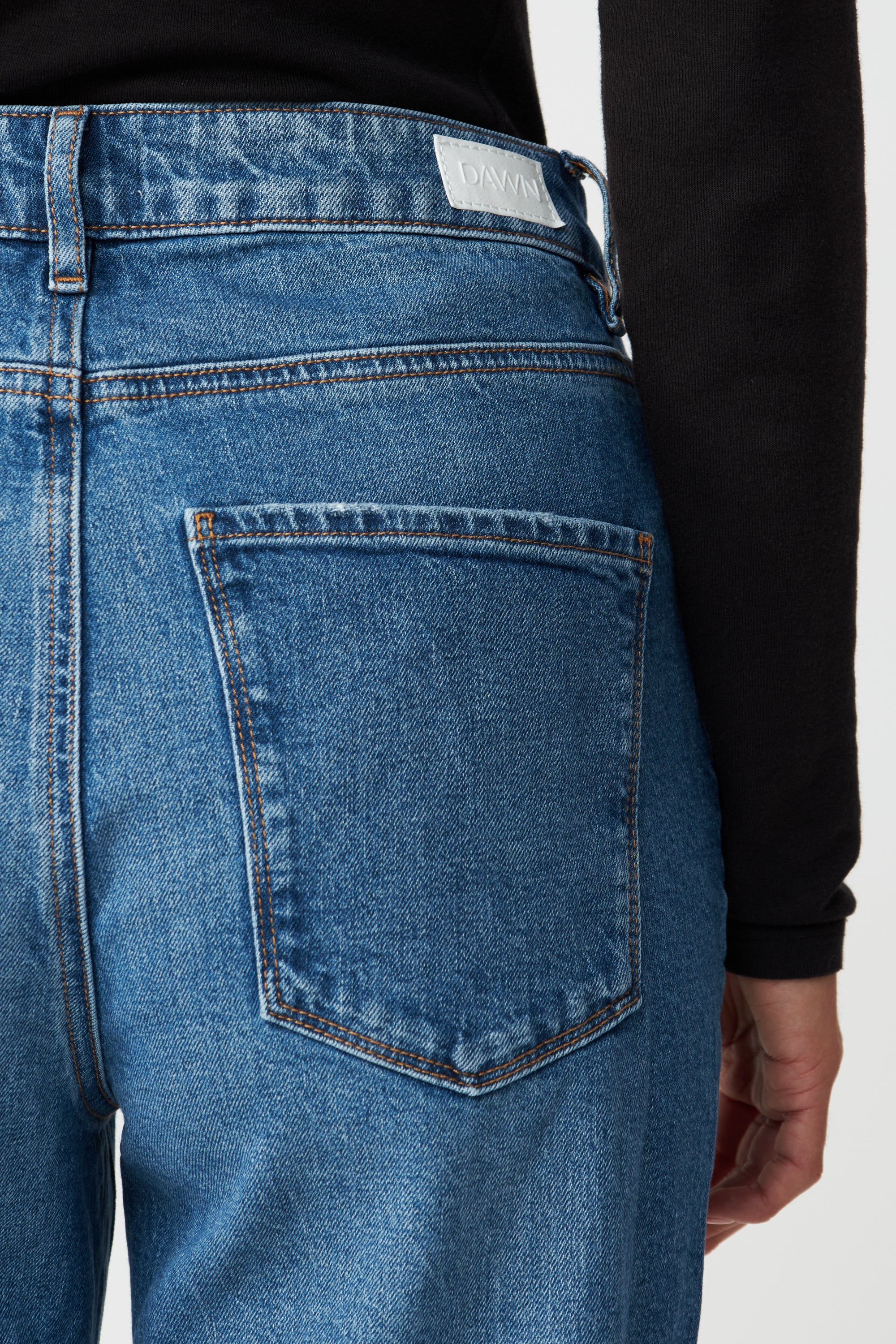 DAWN MORNING Jeans in Medium Blue, Rückansicht mit einer Backentasche, Bund mit DAWN-Label und orange Kontrastnähten.