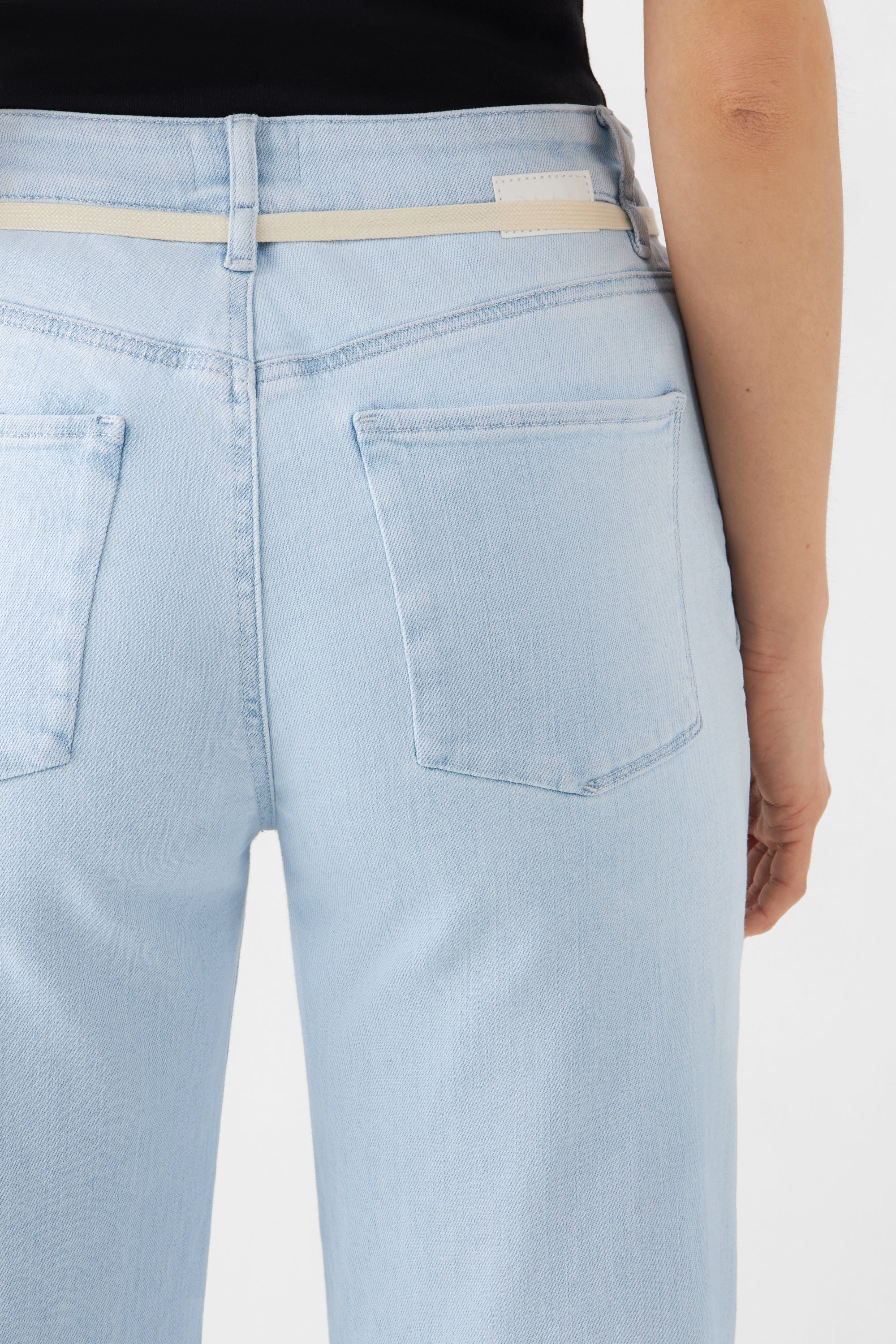 Rückenansicht hellblauer DEW Cropped-Flared-Jeans: hohe Taille, ausgestelltes Bein, französische Taschen, beigefarbener Gürtel.