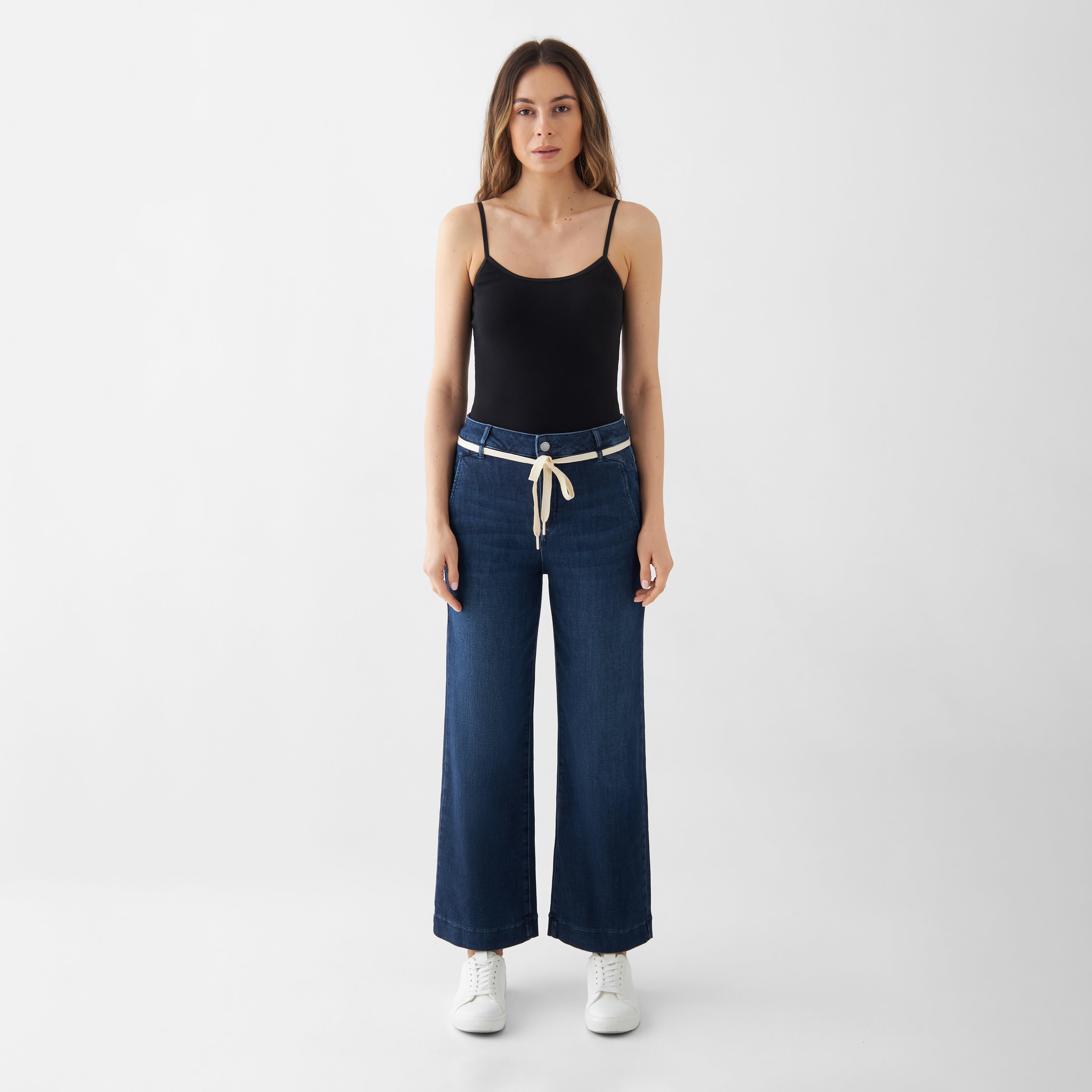 Dunkelblaue DEW Cropped Flared Jeans mit französischen Taschen, High Waist, ausgestelltem Bein; weißer Gürtel.