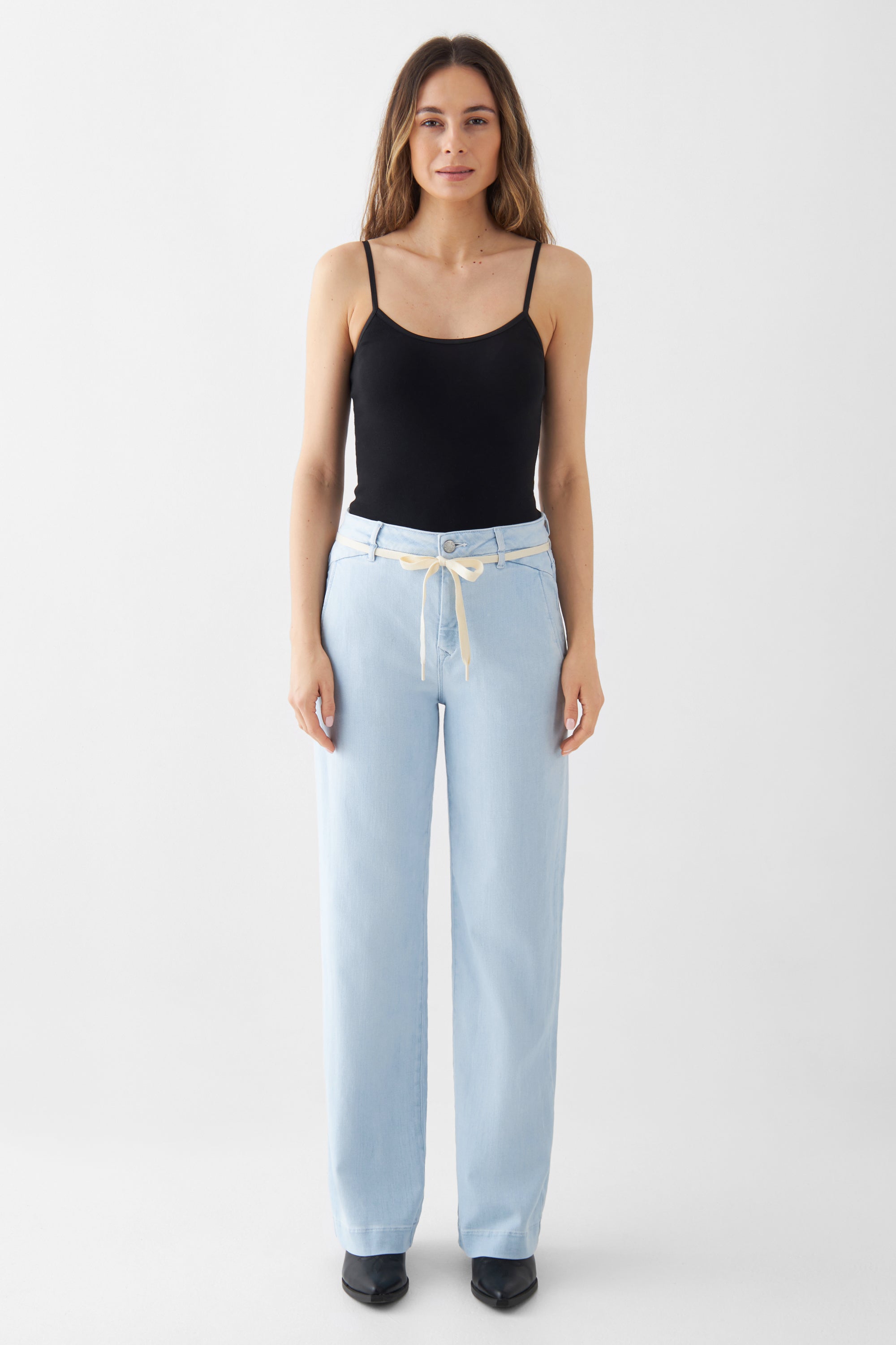 DEW Flared Soft Denim Bright Blue: hoch taillierte, ausgestellte Jeans mit französischen Taschen; Model trägt schwarzes Top und cremefarbenen Gürtel.