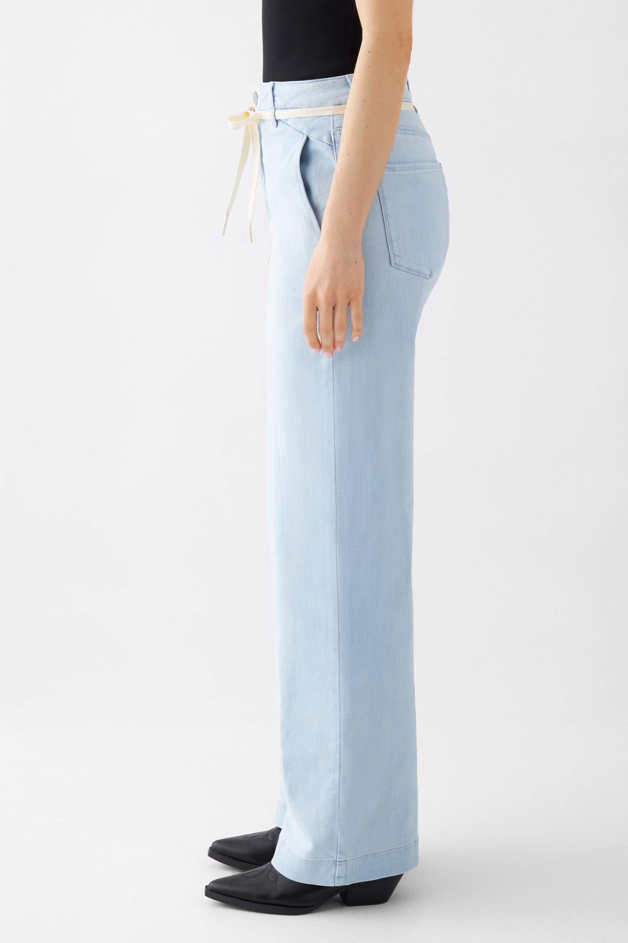 Hellblaue DEW Flared Soft Denim High-Waist-Jeans mit ausgestelltem Bein und französischen Taschen; Seitenansicht mit cremefarbenem Gürtel.
