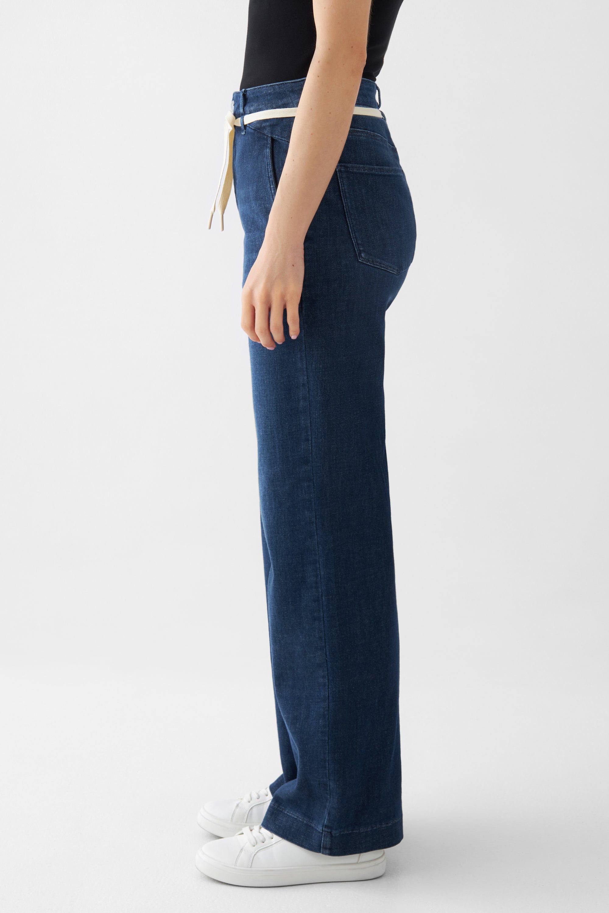 Seitliche Ansicht einer dunkelblauen DEW Flared Soft Denim-Jeans mit französischen Taschen, hoher Taille und ausgestelltem Bein.