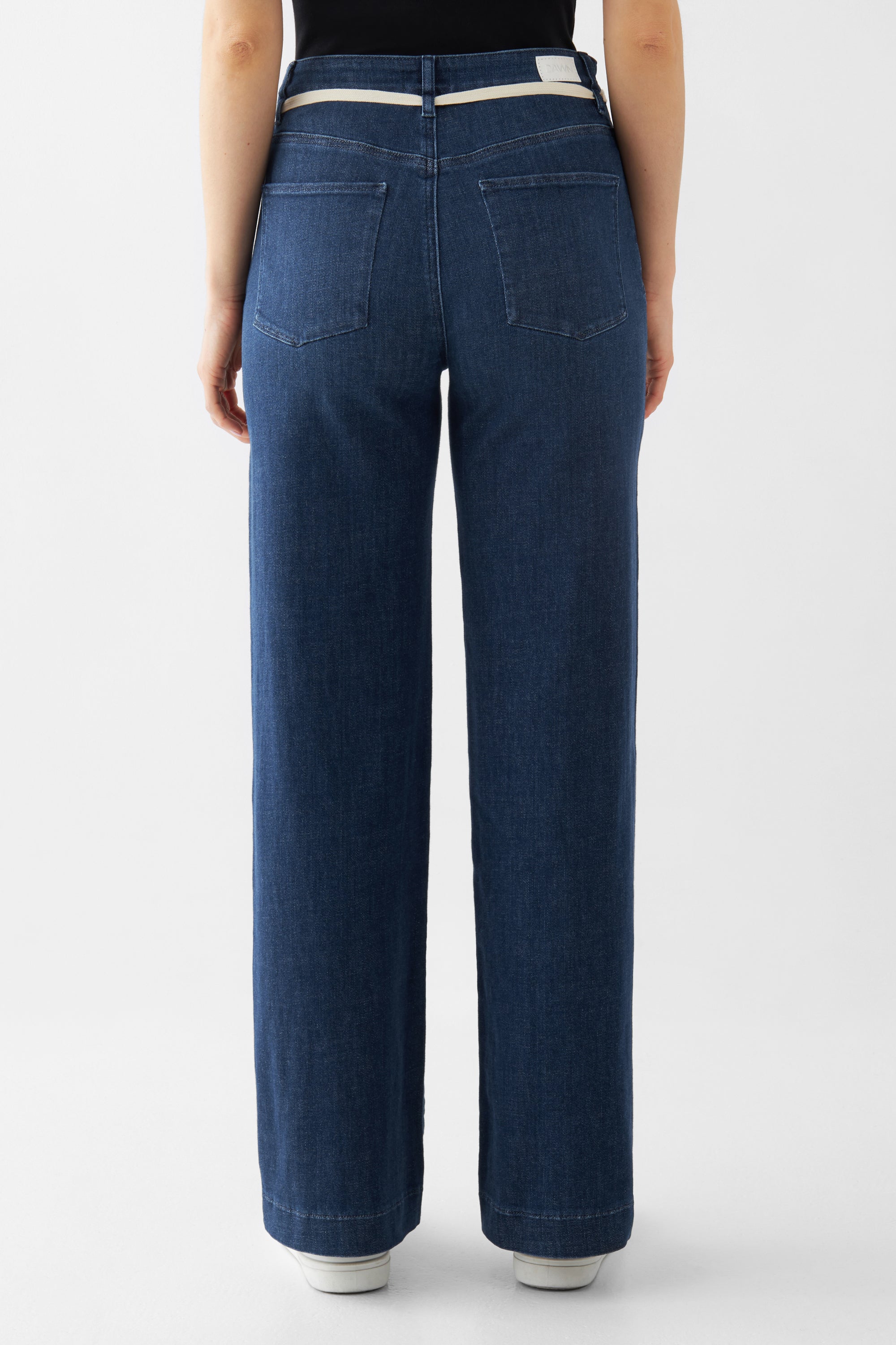 Rückansicht einer dunkelblauen DEW French Pocket Jeans mit hoher Taille, ausgestelltem Bein und zwei Gesäßtaschen; heller Gürtel am Bund.