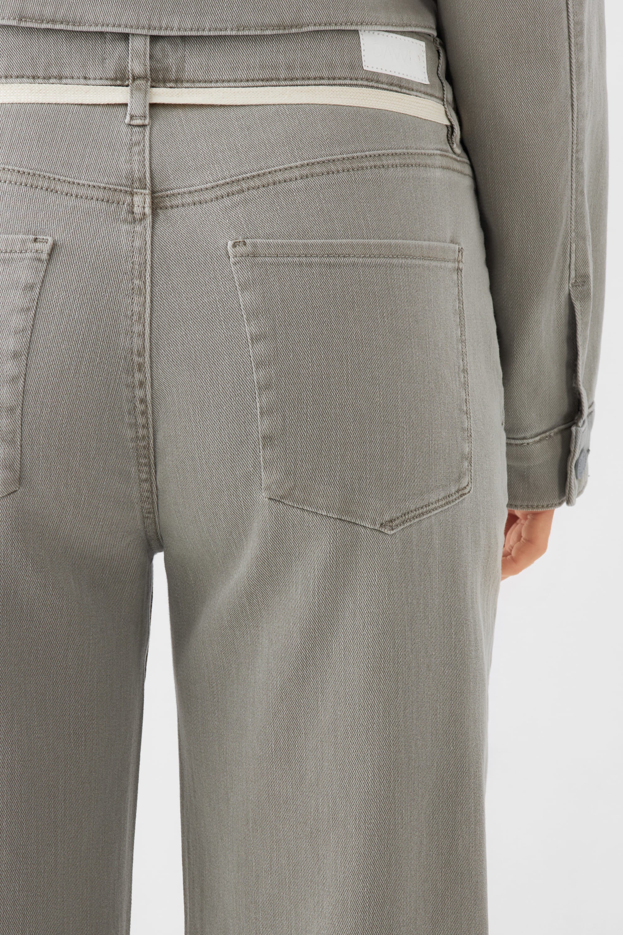 Rückenansicht einer DEW High-Waist Jeans in Rock Olive mit französischen Taschen und ausgestelltem Bein.