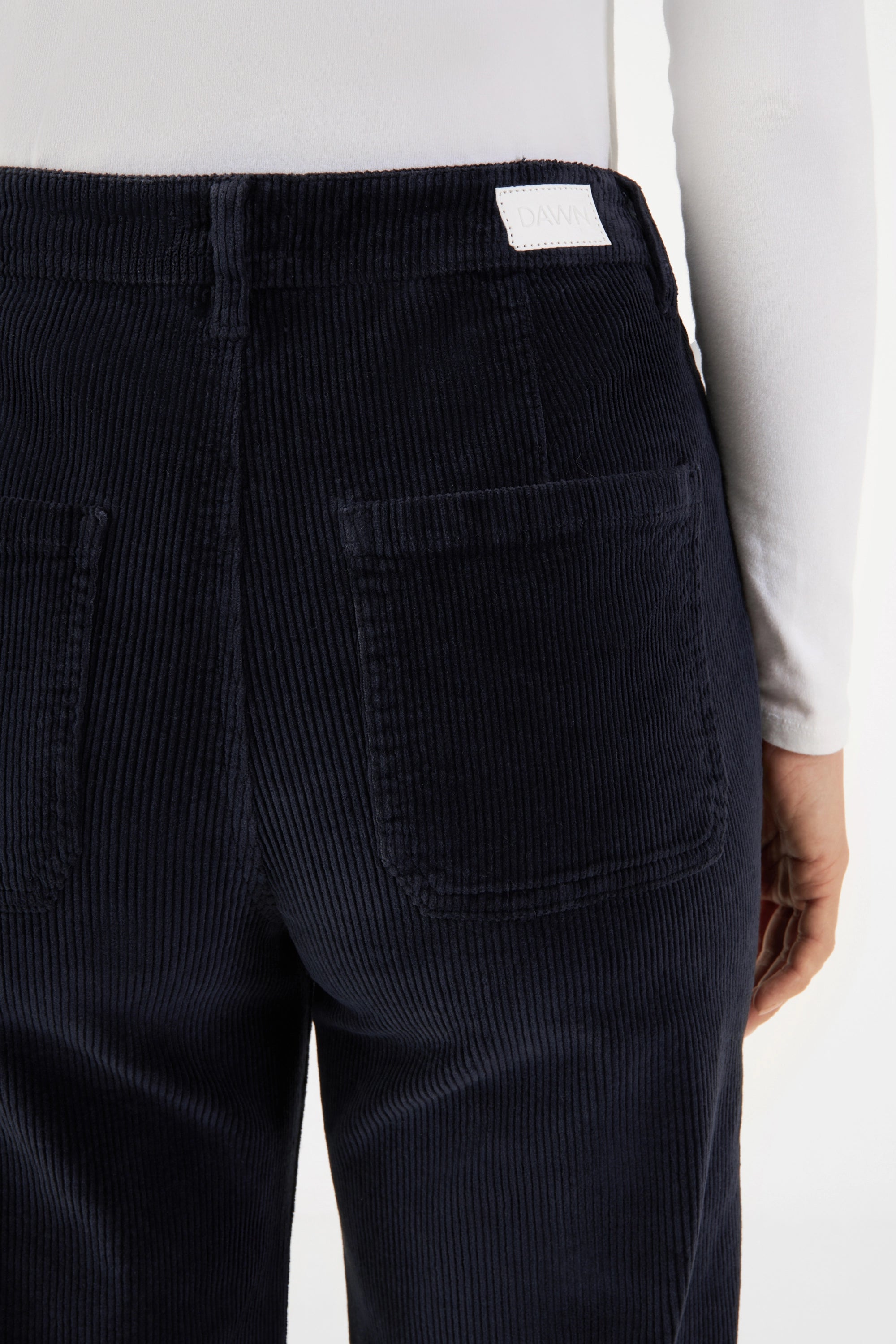 Rückenansicht: dunkelblaue DEW Sailor Cordhose, hoher Bund, zwei Rückentaschen, weißes DAWN-Label am Bund – Cord-Stoff.