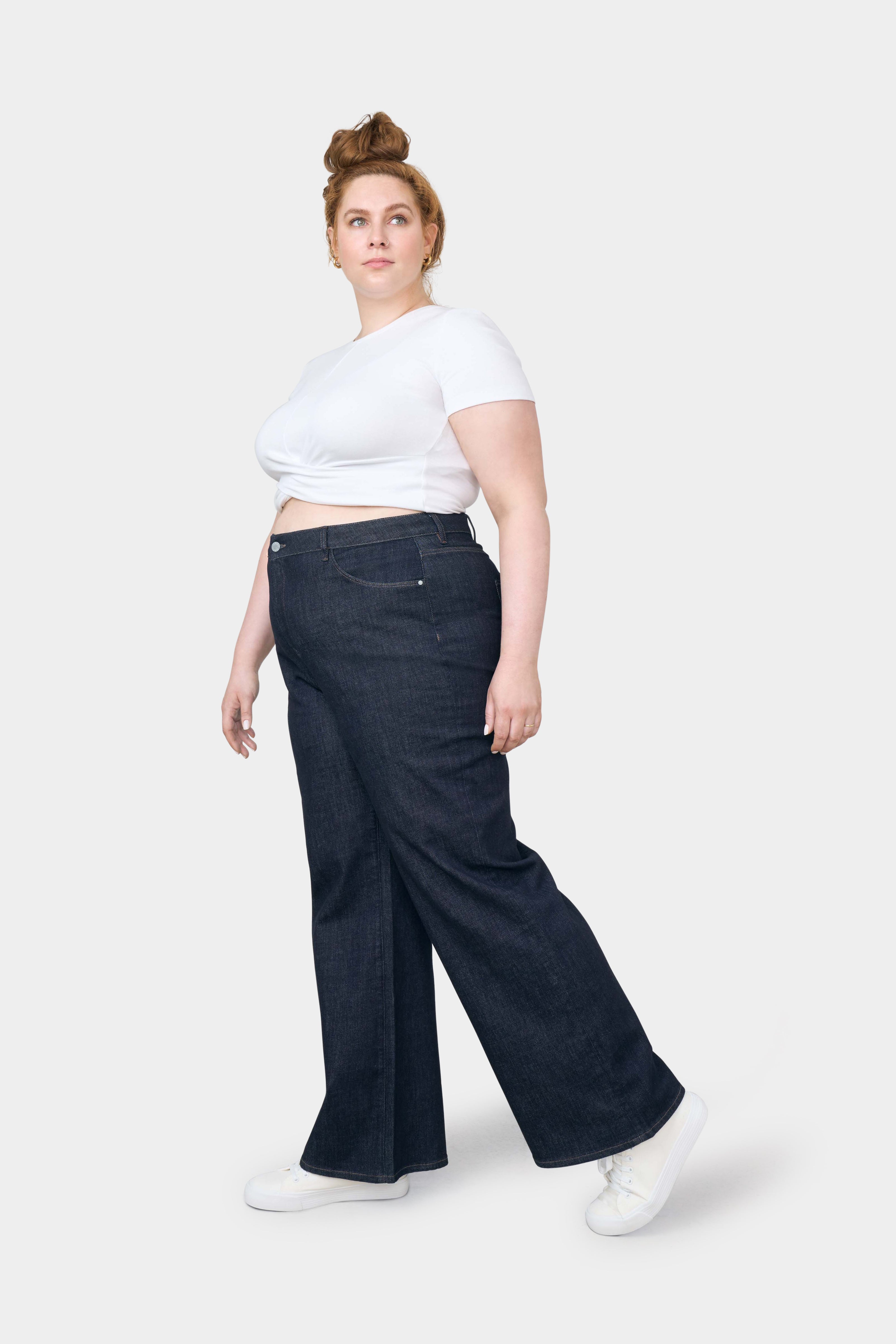 DEW Flared Soft Denim in Raw Blue: High-Waist, ausgestelltes Bein, bequemer Stretch-Denim; getragen von einer kurvigen Frau in weißem Top.