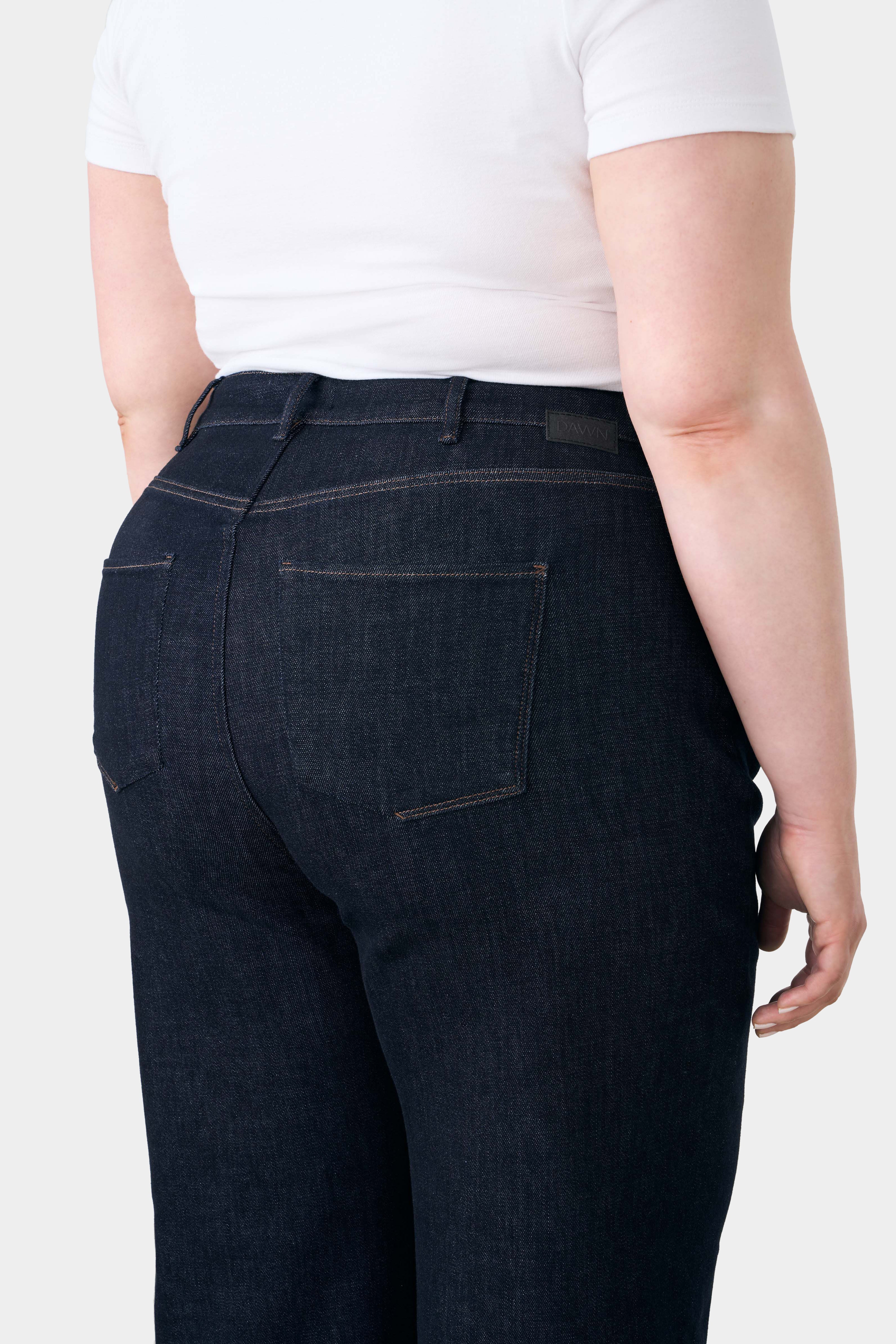 Rückansicht einer High-Waist-Jeans in Raw Blue mit ausgestelltem Bein; 5-Pocket-Design, Kontrast-Nähte, DAWN-Label am Bund.