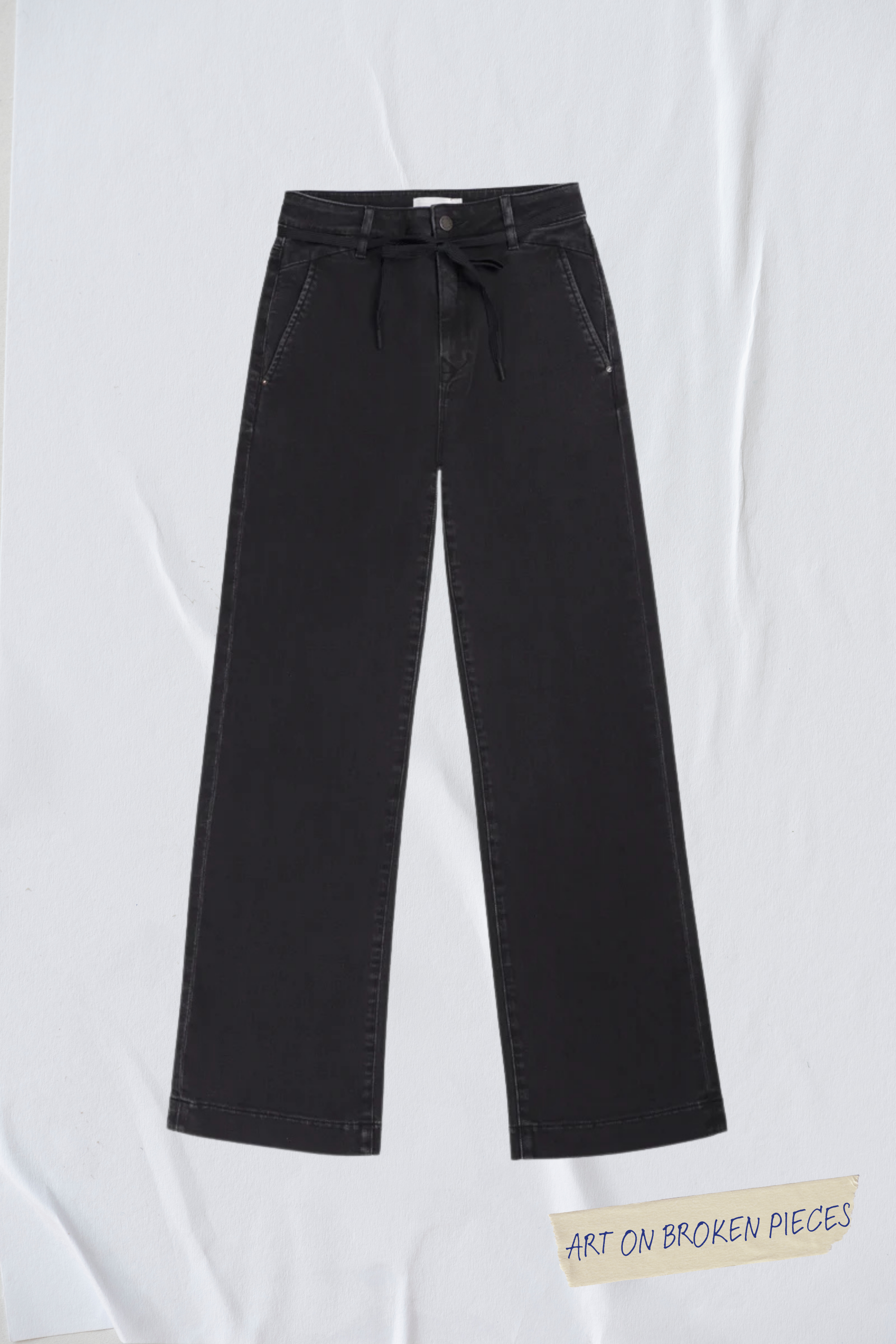 Schwarze DEW Cropped Flared Jeans mit hohem Bund, französischen Taschen und Bindegürtel; ausgestelltes Bein, Label ‚Art on Broken Pieces‘ am unteren Rand.