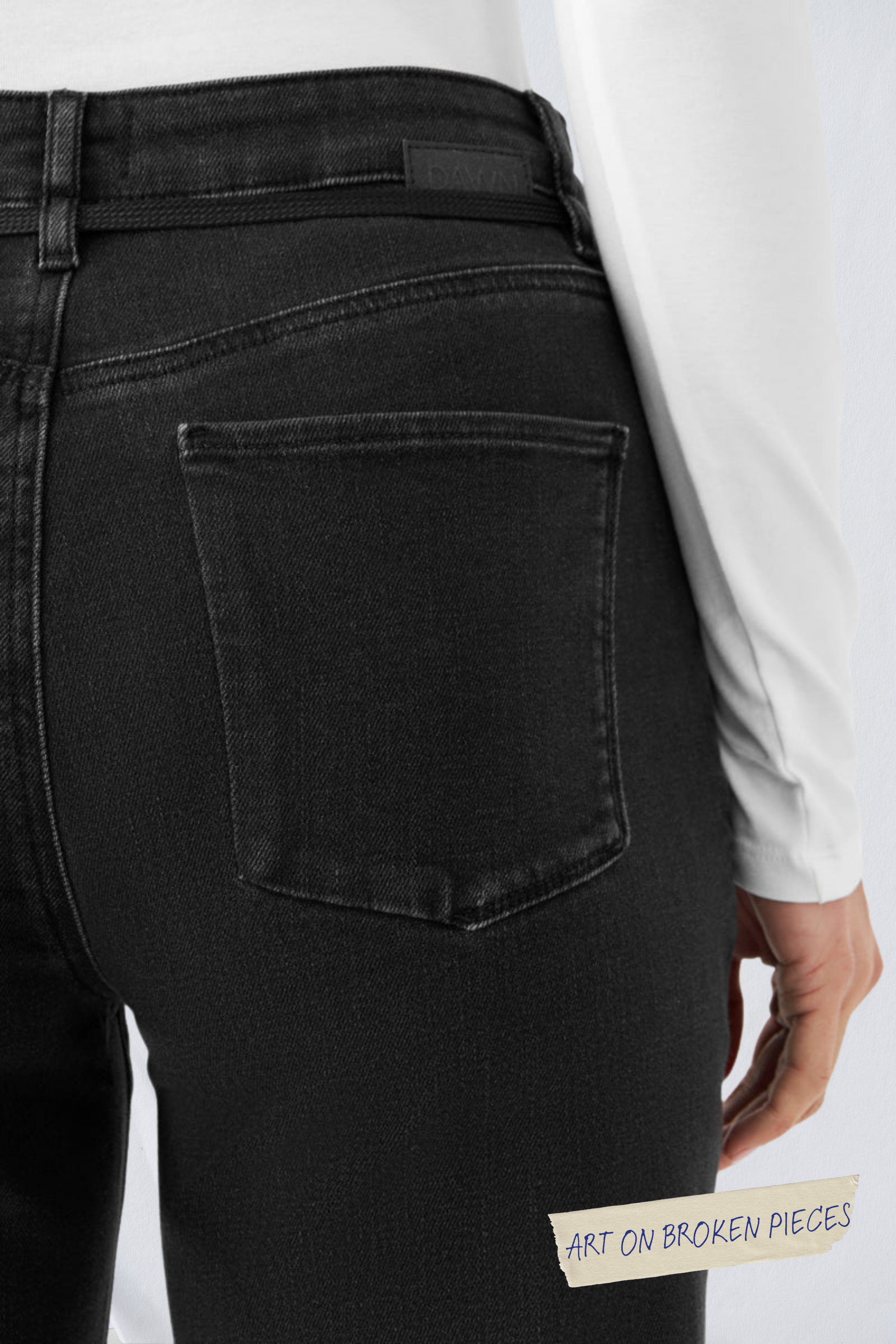 Schwarze DEW Cropped Flared Jeans mit French Pocket, hohem Bund und ausgestelltem Bein; sichtbare Rückentasche, Art on Broken Pieces-Aufkleber am Stoff.