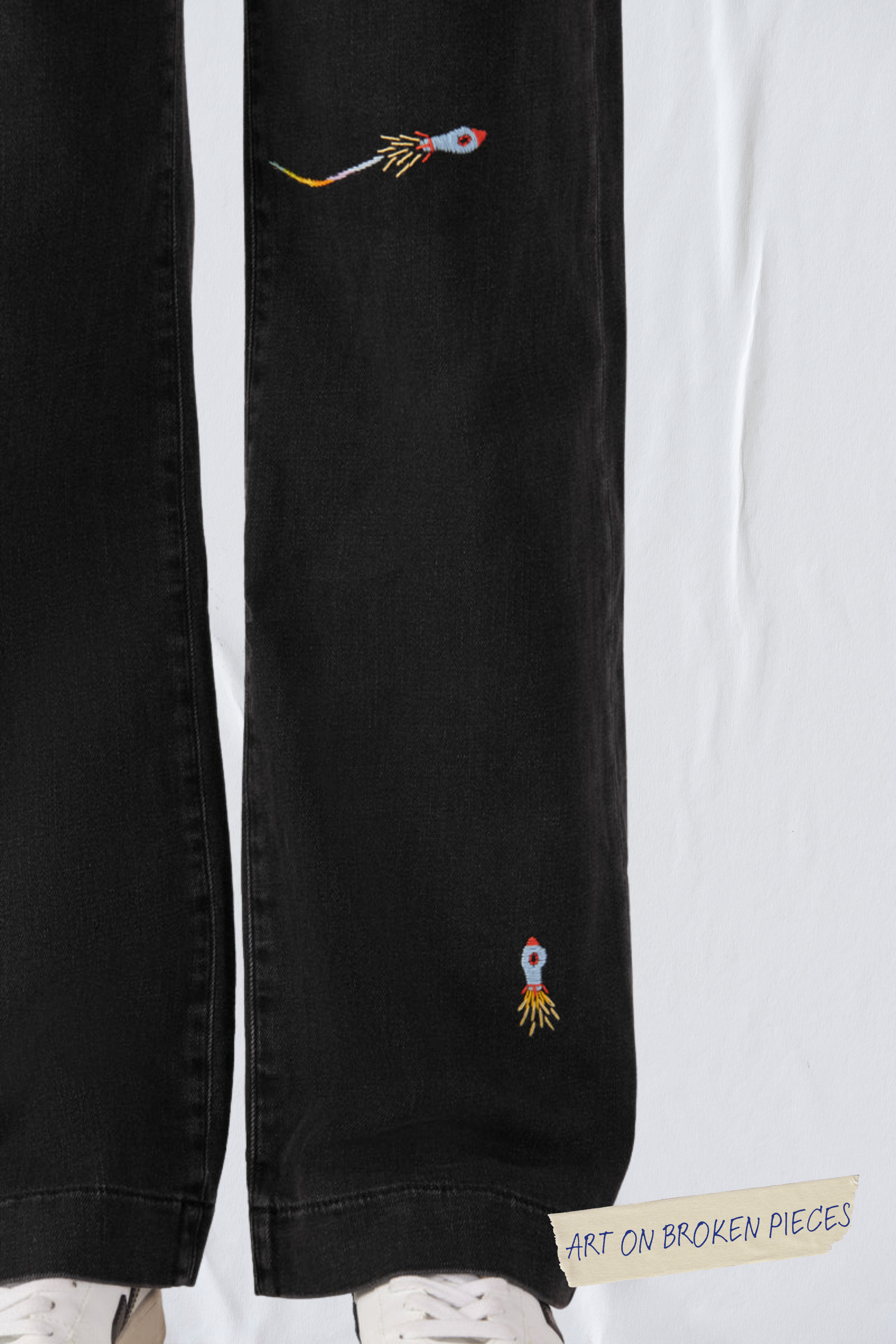 Schwarze DEW Flared-Jeans; französische Taschen, Unikat Art on Broken Pieces mit zwei Raketen-Stickereien am Oberschenkel und Knöchel.