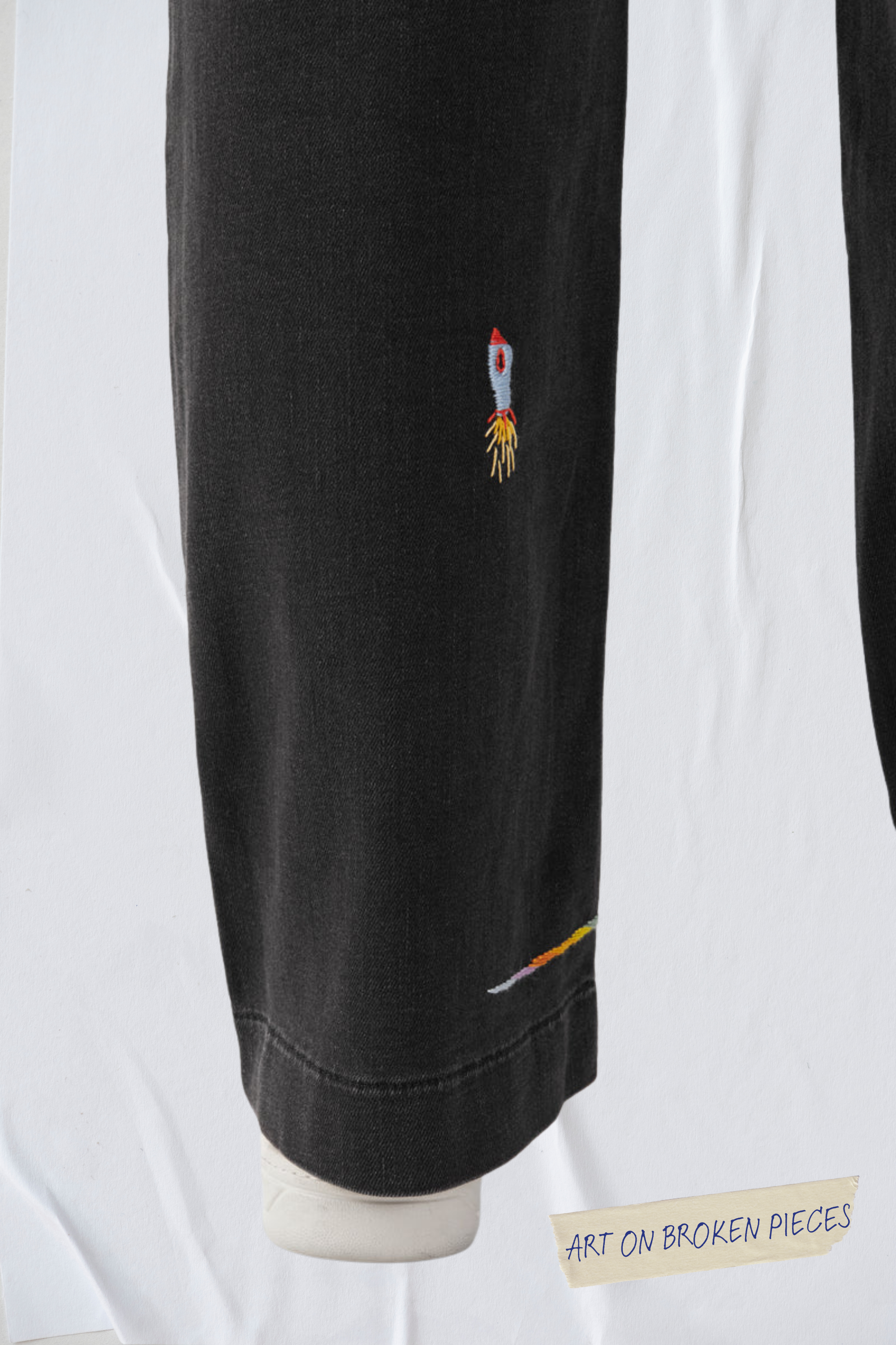 Schwarze DEW Flared Soft Denim Jeans mit French Pocket; Raketen-Stickerei am Oberschenkel und bunte Saumlinie – Art on Broken Pieces.