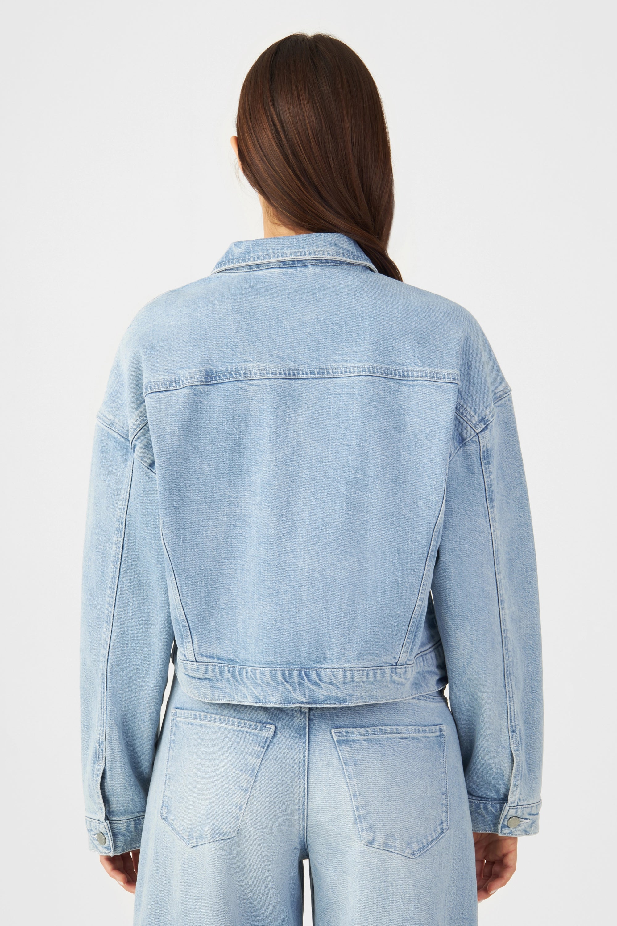 Rückansicht einer hellblauen, kurzen Boxy-Denimjacke mit Kragen, überschnittenen Schultern und sichtbaren Nähten.