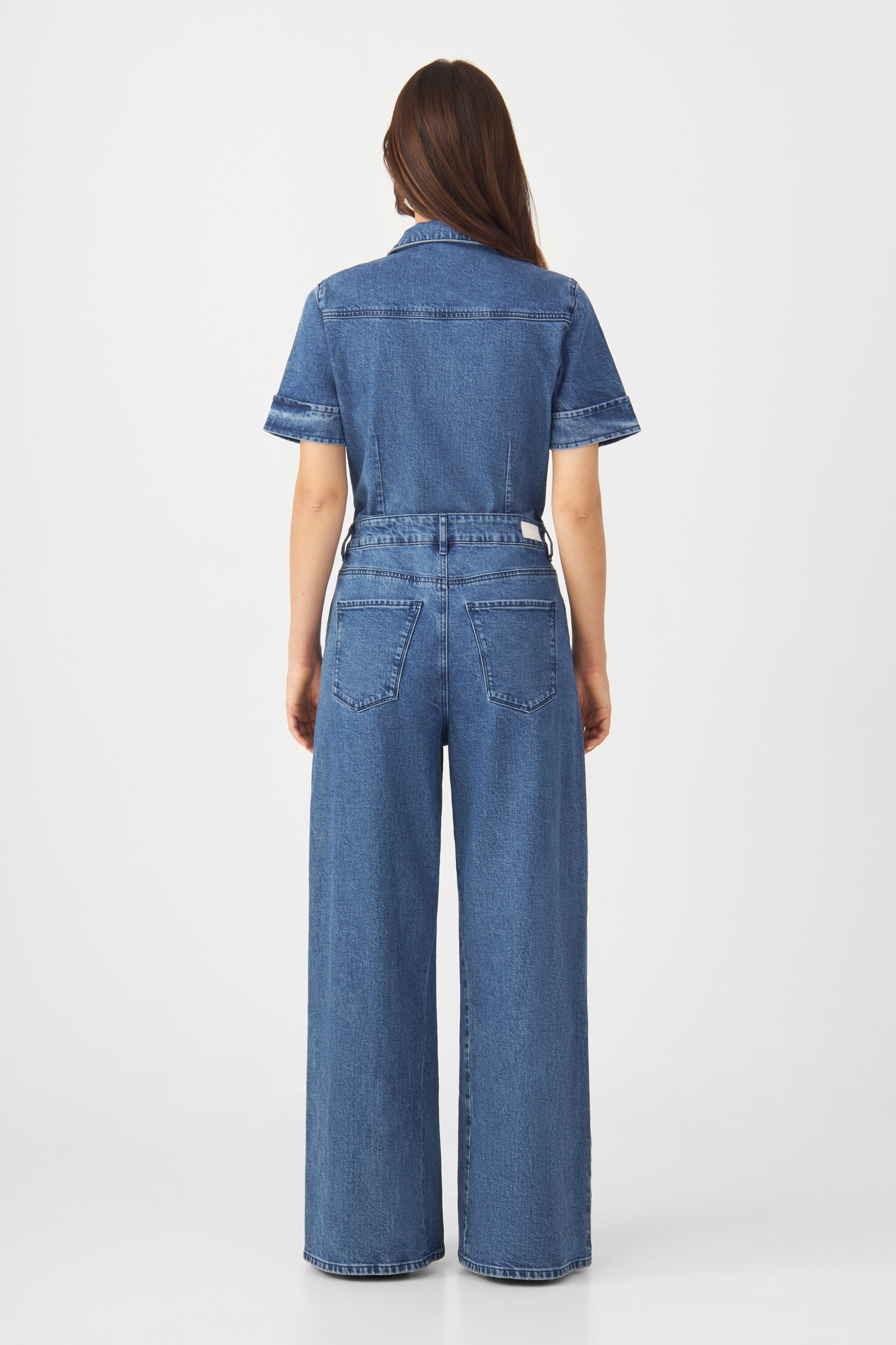 Rückansicht eines mittelblauen Denim-Overalls mit kurzen Ärmeln, taillierter Passform, weitem Bein und zwei Gesäßtaschen.