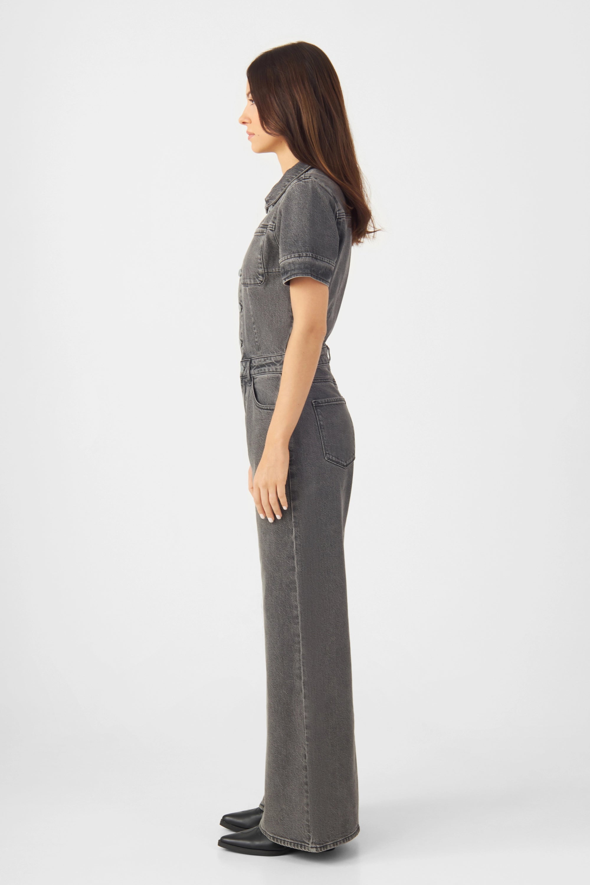 Dunkelgrauer Denim-Overall mit kurzen Ärmeln, enger Taille, weiter Beinform und aufgesetzten Brusttaschen; seitliche Modelansicht.