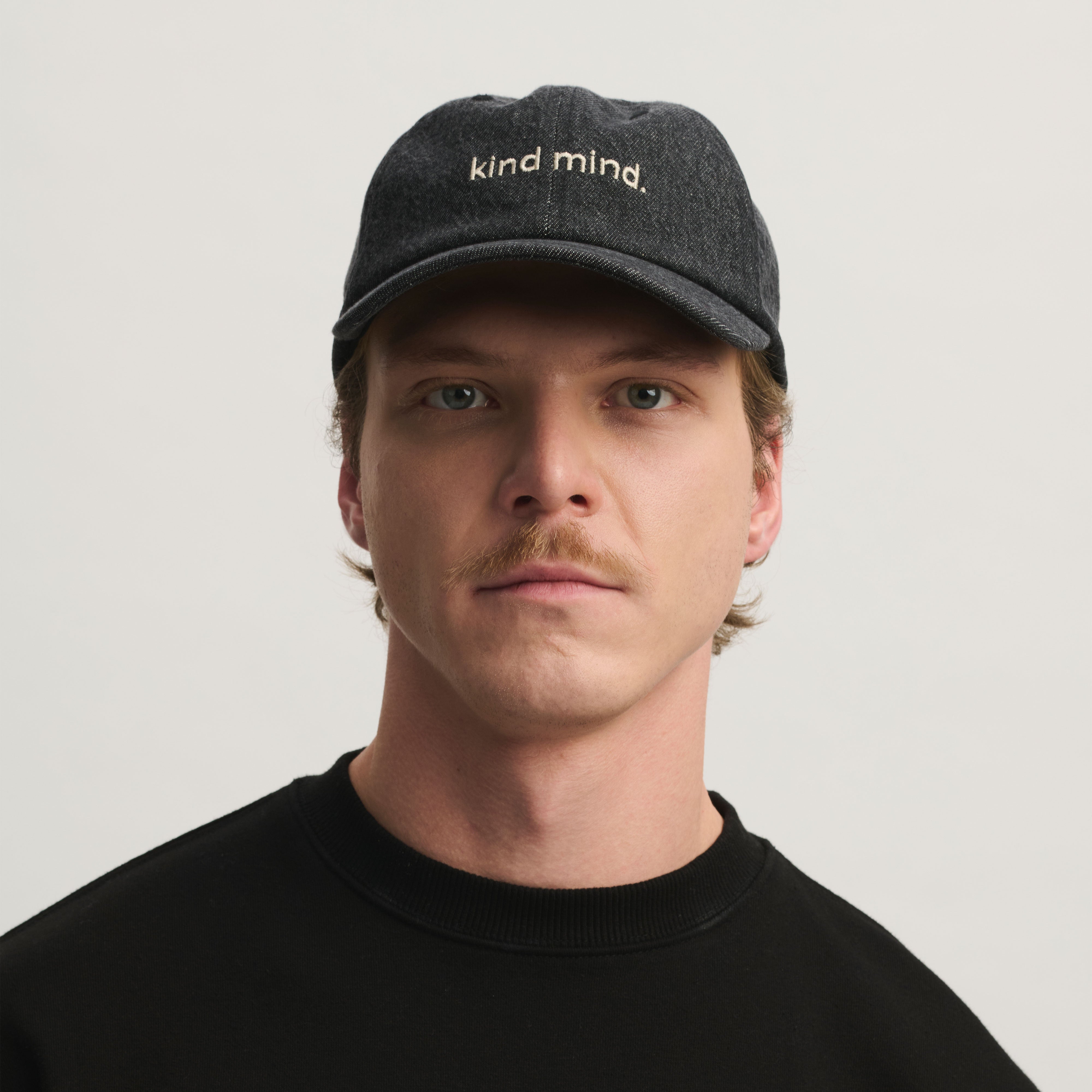 Frontansicht eines Mannes mit dunkelgrauer Denim-Cap, 'kind mind.' Logo vorne; Cap aus Bio-Baumwolle, Limited Edition.