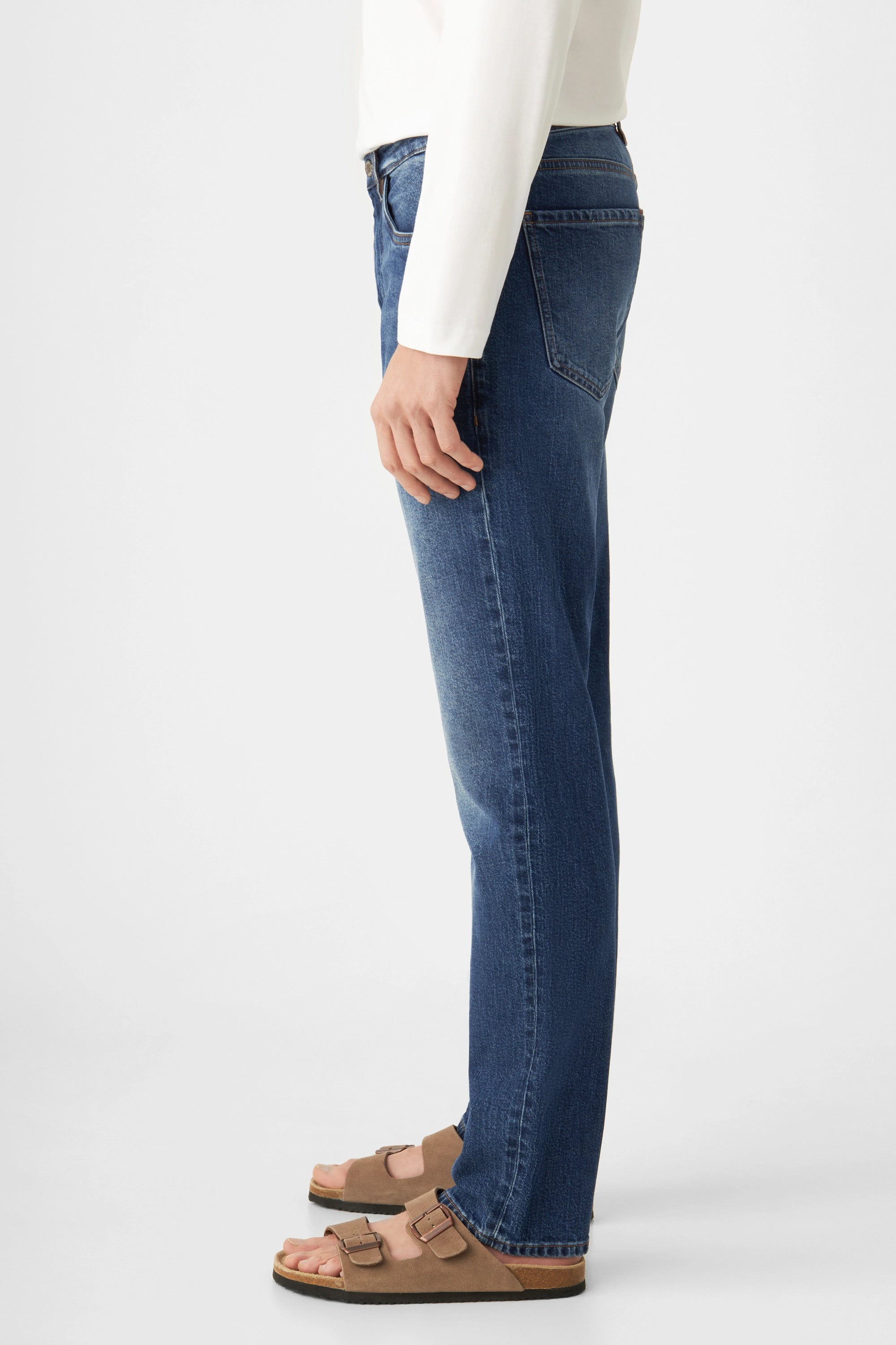 Seitenansicht einer dunkelblauen DUSK Jeans – Regular Straight mit mittlerer Taille und geradem Bein; Modell trägt weißes Oberteil und Sandalen.