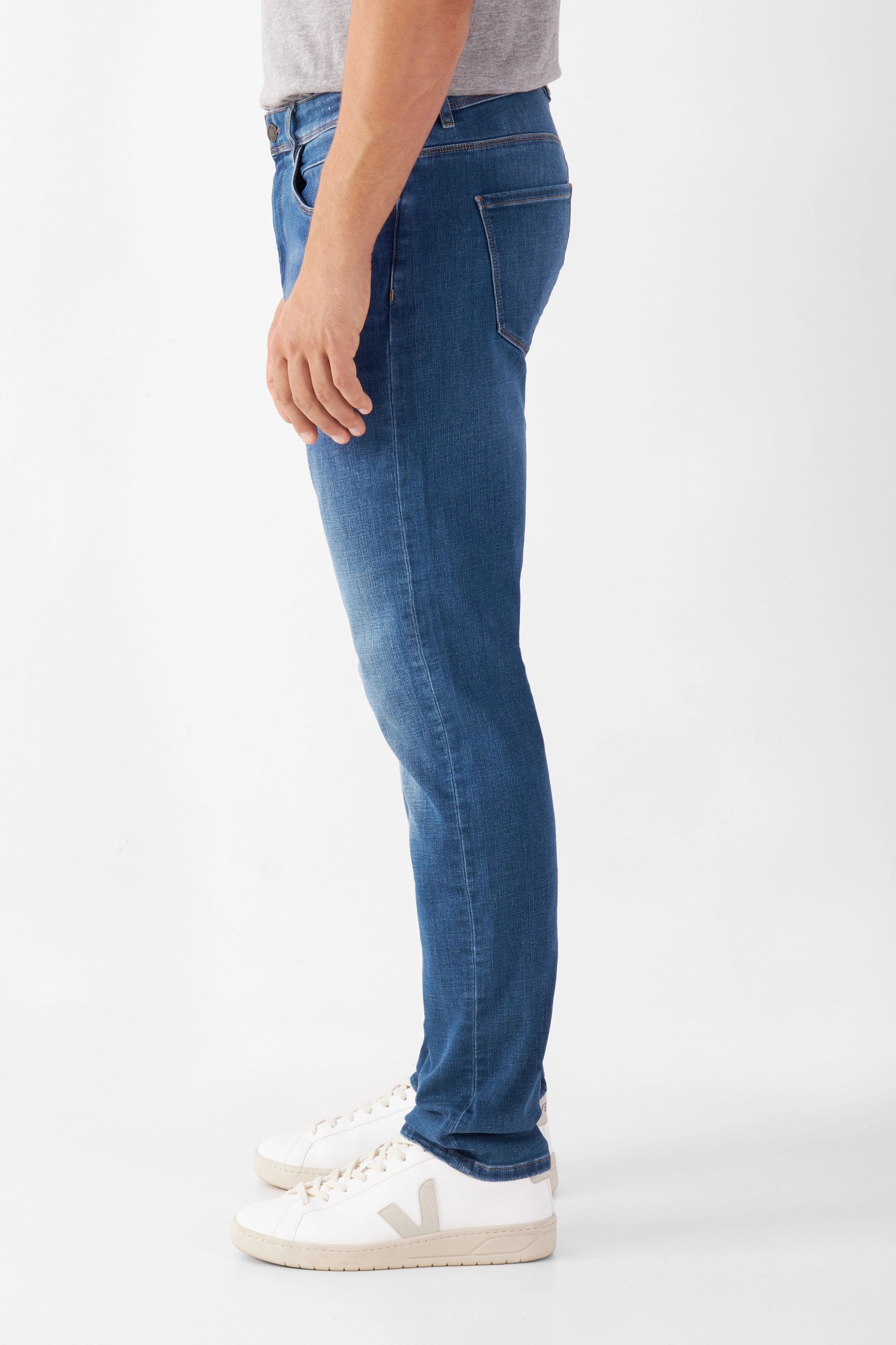 Seitenansicht der MORROW Slim Fit Jeans in Medium Blue; mittlere Taille, leicht zulaufendes Bein, Komfortstretch; Modell trägt weiße Sneaker.