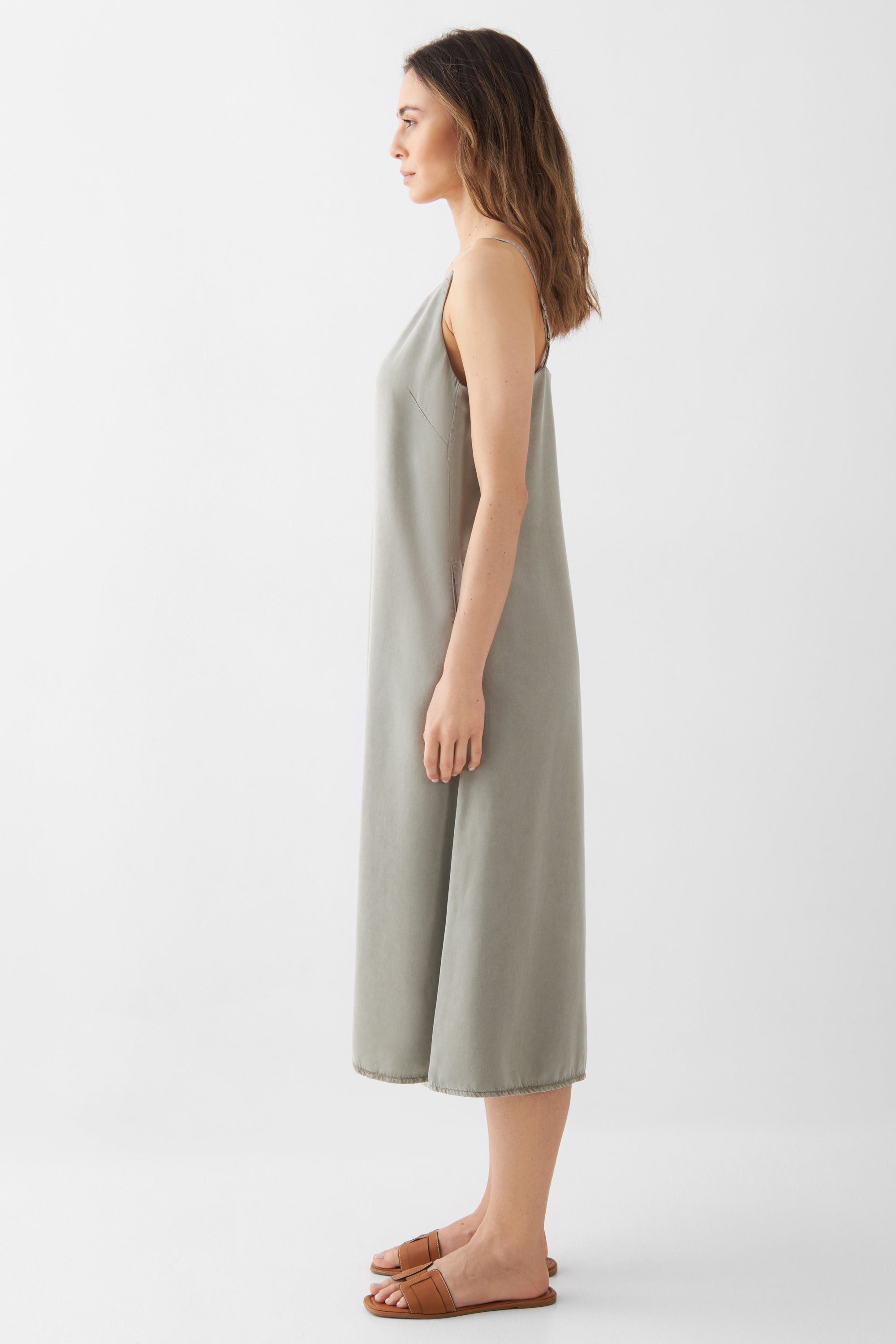 Seitenansicht einer Frau im SUNBEAM Rock Olive Midikleid aus Lyocell (TENCEL™), V-Ausschnitt, verstellbare Träger, lockere A-Linien-Silhouette mit seitlichen Taschen.