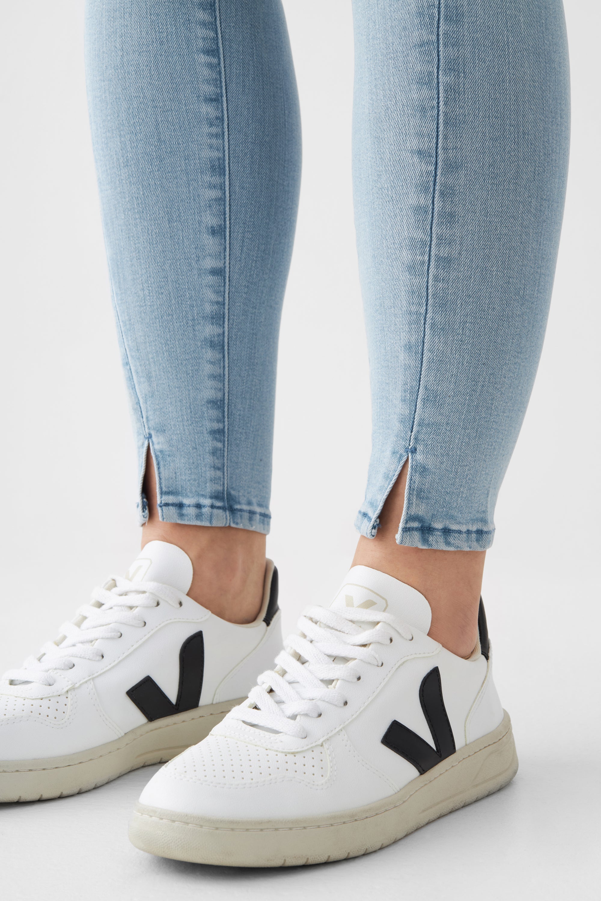 Hellblaue SUN UP Skinny Powerstretch Jeans, knöchellang mit Saumschlitz und schräger Außennähte, getragen zu weißen Sneakern.