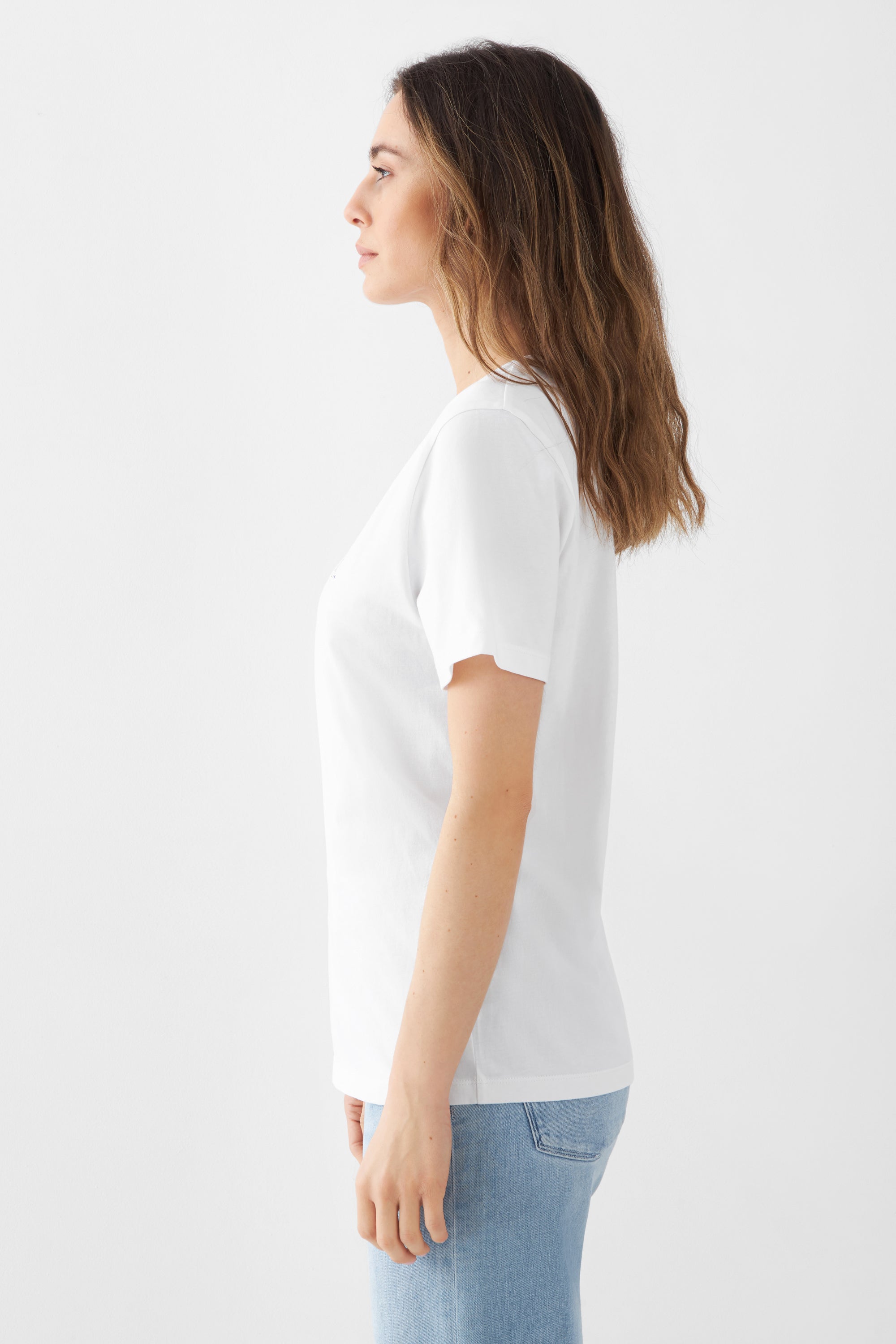 Seitenansicht einer Frau in einem weißen, kurzärmligen Rundhals-T-Shirt von DAWN; Unisex-Fit, 100% Bio-Baumwolle, kombiniert mit hellblauen Jeans.