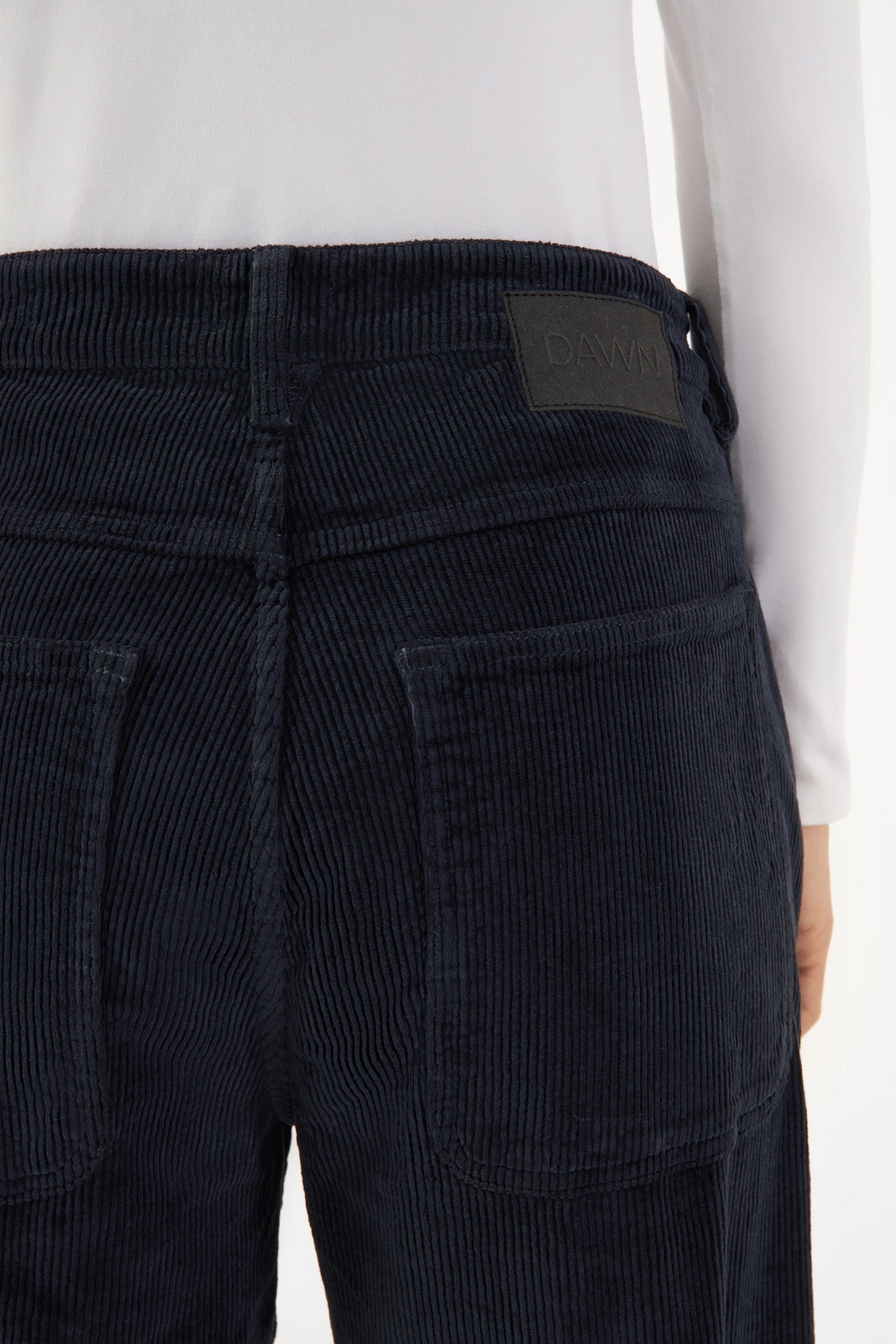 Dunkelblaue Corduroy-Hose MANE Relaxed Straight für Damen, Rückansicht mit zwei Gesäßtaschen und mittelhohem Bund; DAWN-Logo-Patch am Bund.