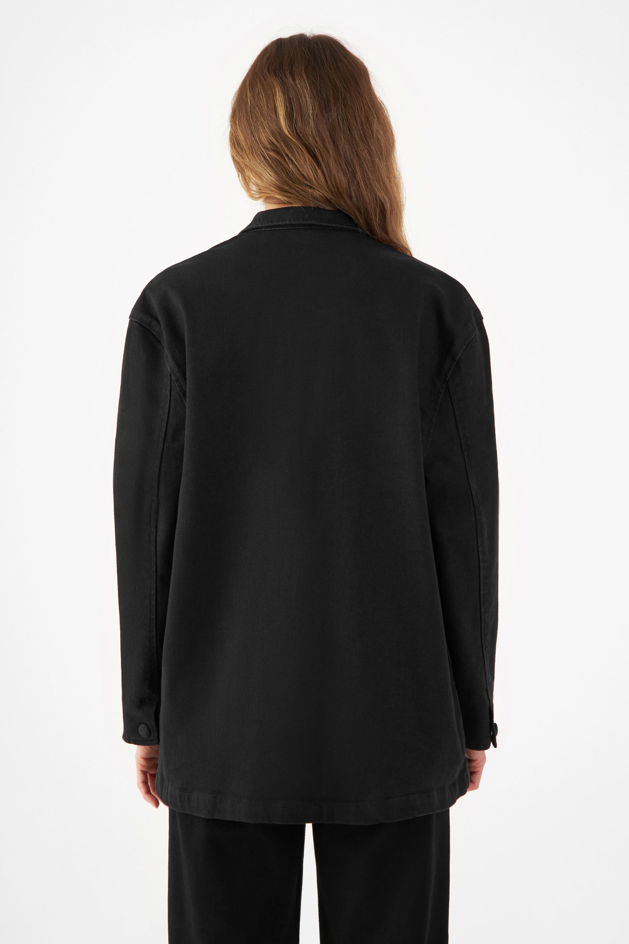 Rückenansicht einer schwarzen QUIET Jacke aus Lyocell‑TENCEL Denim, kastig-locker, komplett gefüttert, stoffbezogene Druckknöpfe.