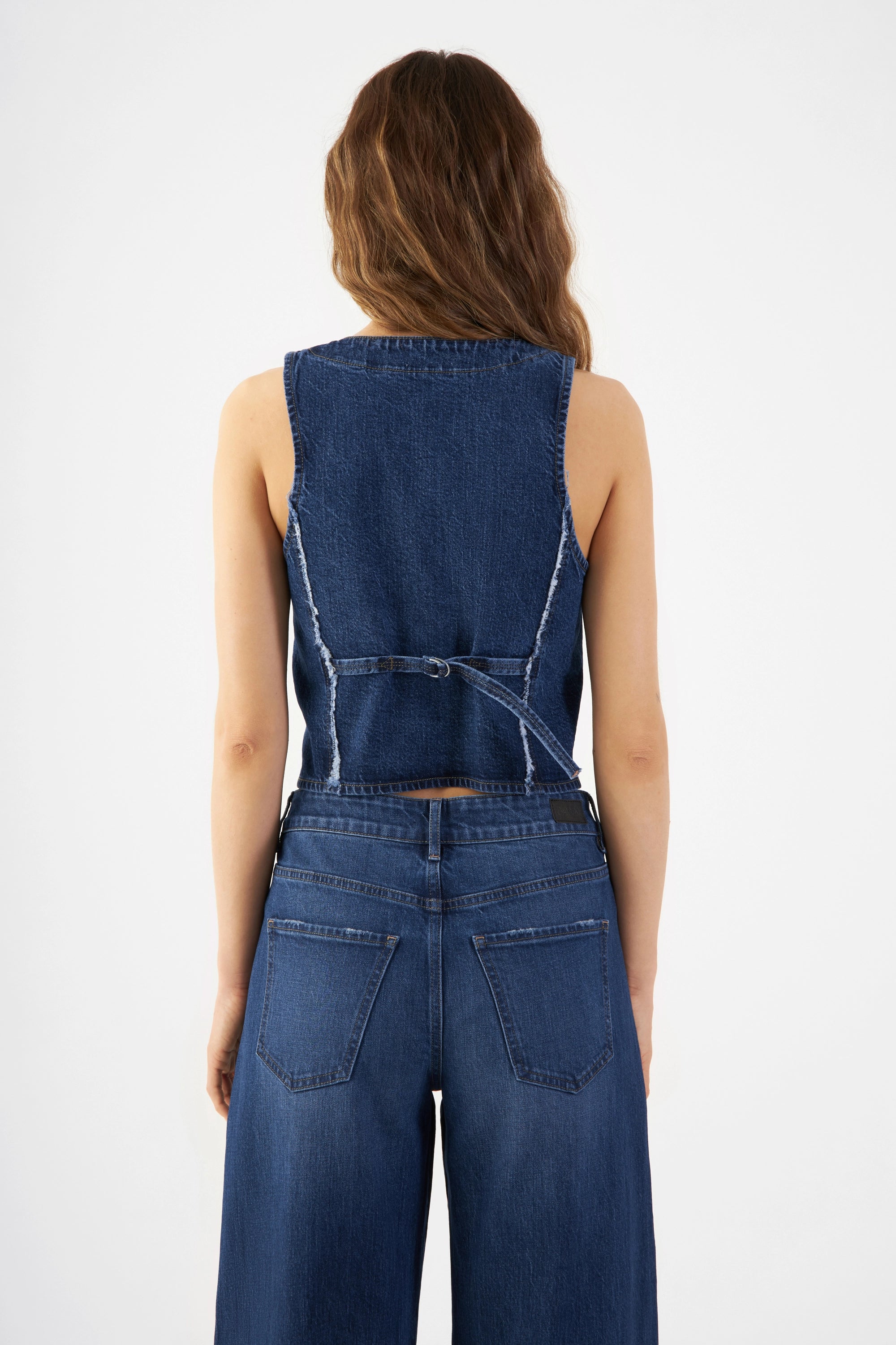 Rückansicht einer dunkelblauen, taillierten Denim-Weste ohne Ärmel mit ausgefransten Kanten.