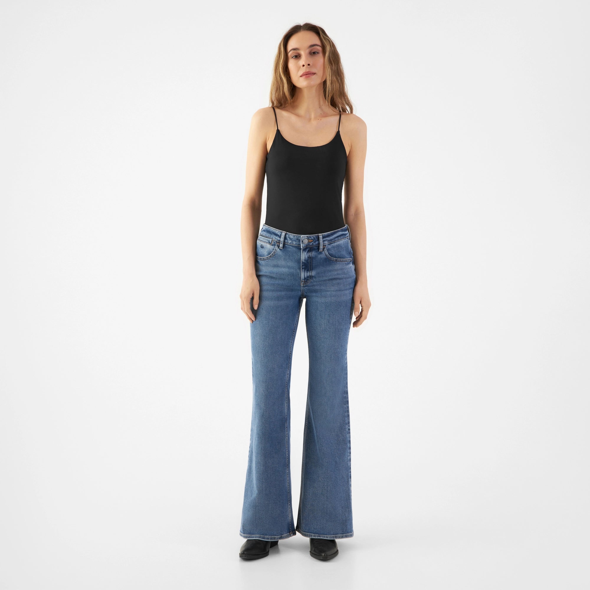 Frontansicht: CELESTIAL Slim Flared Jeans Medium Blue, mittelhoher Bund, schmal bis Knie, ab Knie ausgestelltes Bein, Taschen, schwarzes Top.