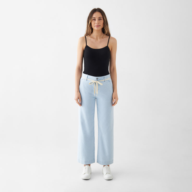 hellblaues, hoch tailliertes DEW Cropped Jeans mit ausgestelltem Bein und französischen Taschen; beiger Kordelgürtel, kombiniert mit schwarzem Top und weißen Sneakern.