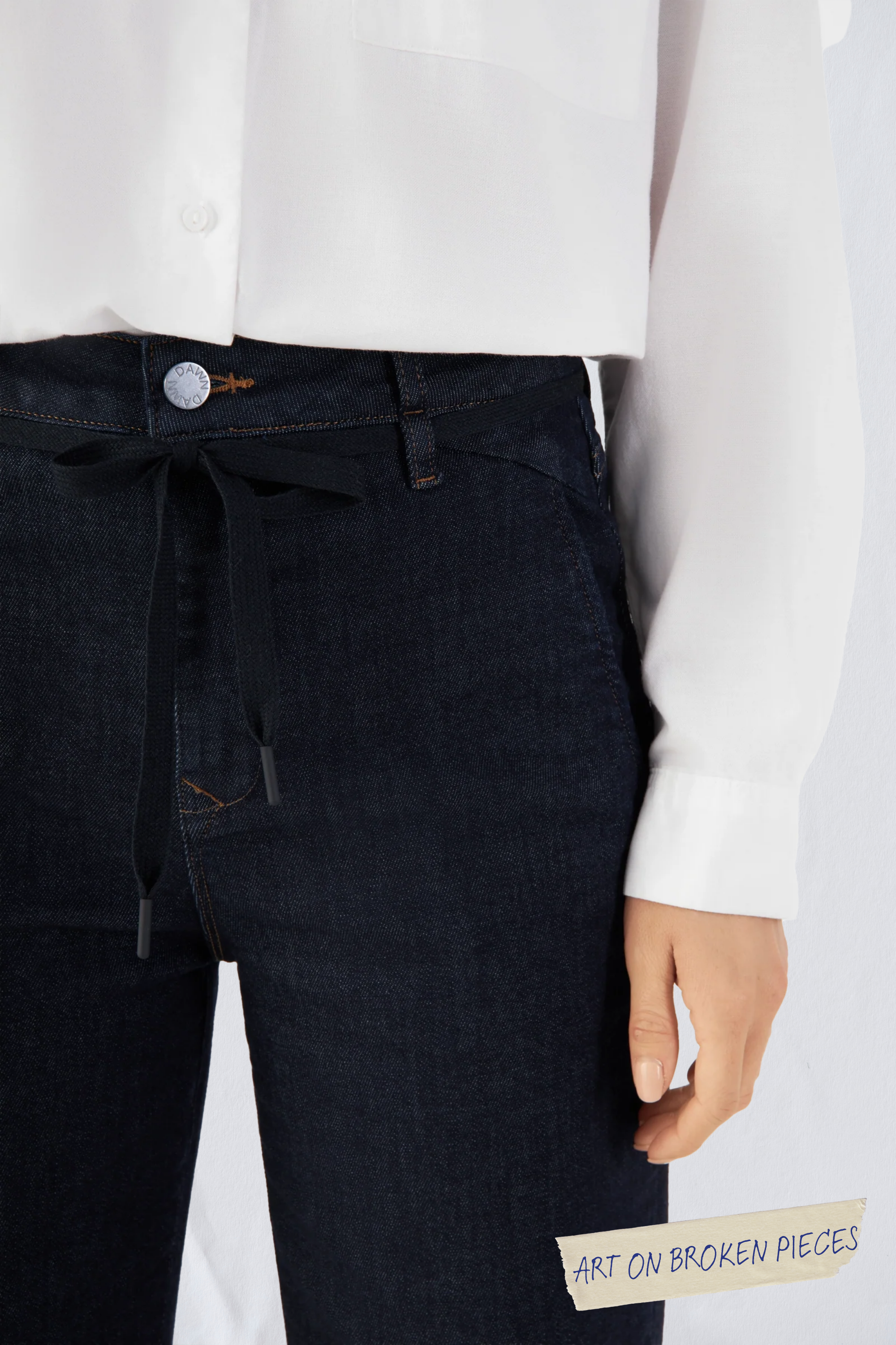 Raw Blue DEW Cropped Flared Jeans mit Kordelzug-Taille und französischen Taschen; hochsitzt, ausgestelltes Bein, Art on Broken Pieces-Aufnäher sichtbar.