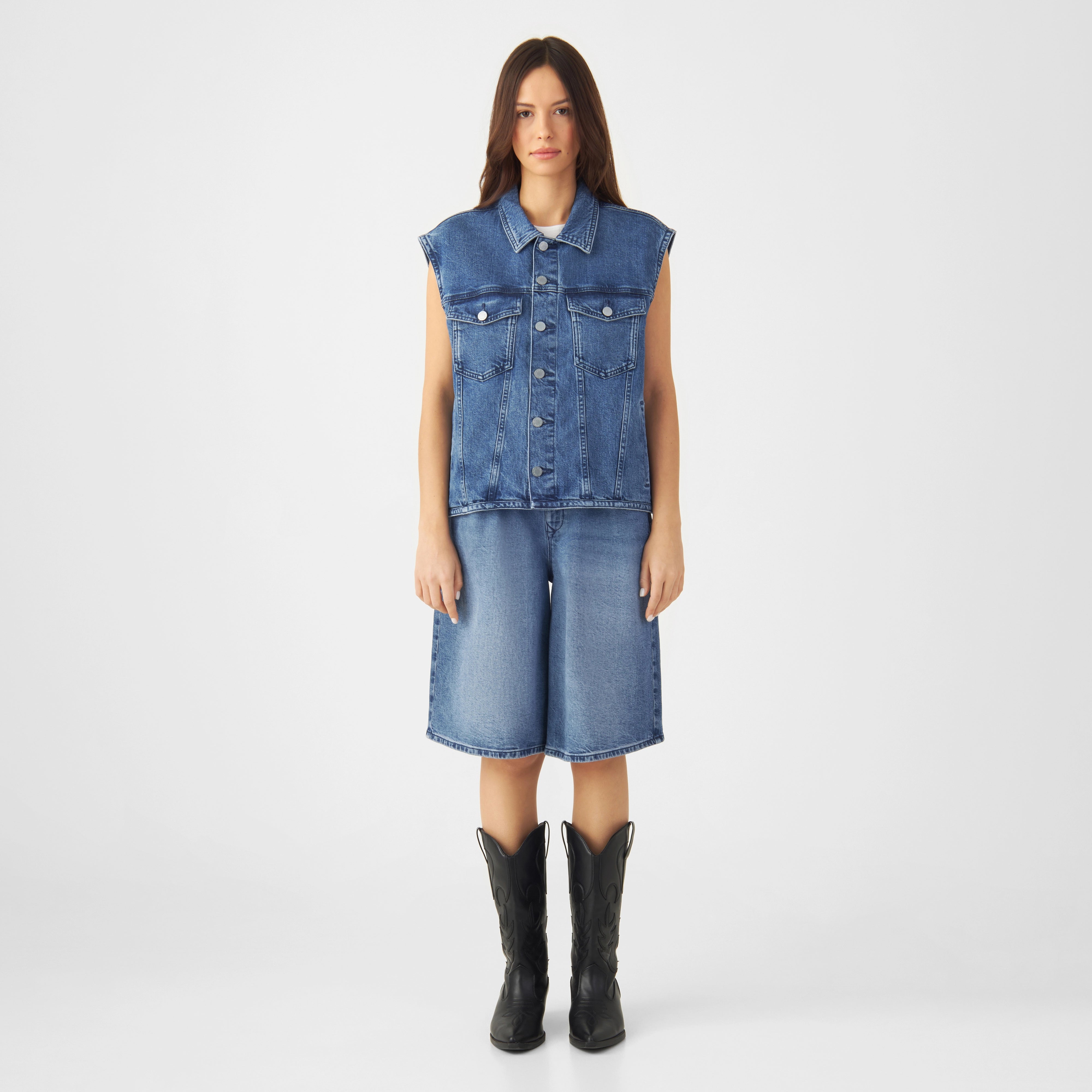Frontansicht einer Frau in der LUNAR Minimal Stretch Denim-Weste in Medium Blue: ärmellose Jacke mit Button-Front und Brustklappentaschen.