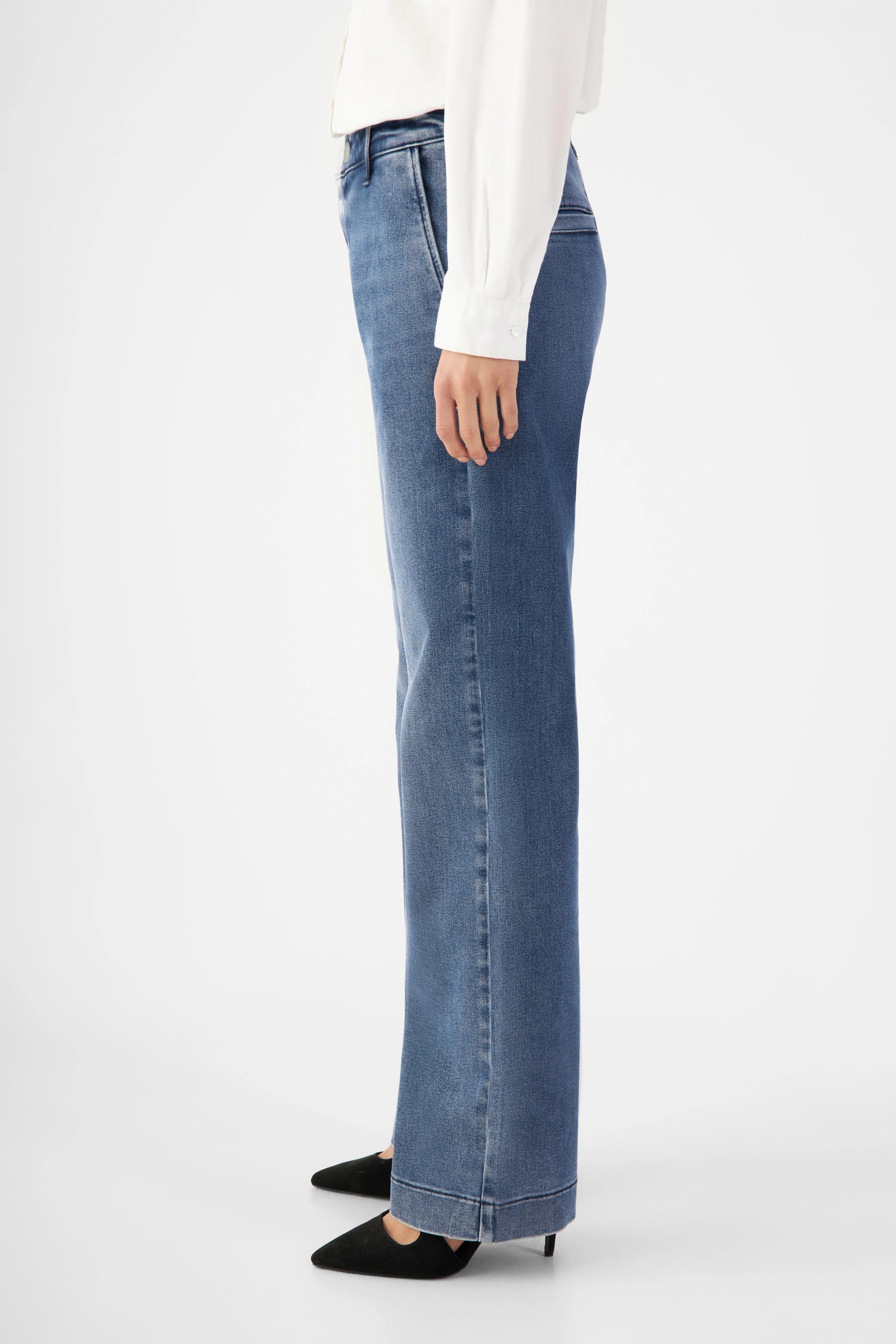 Seitenansicht einer mittelblauen GLOW Denim-Chino mit mittelhoher Taille und ausgestelltem Bein; vorne französische Taschen, hinten Paspeltaschen.
