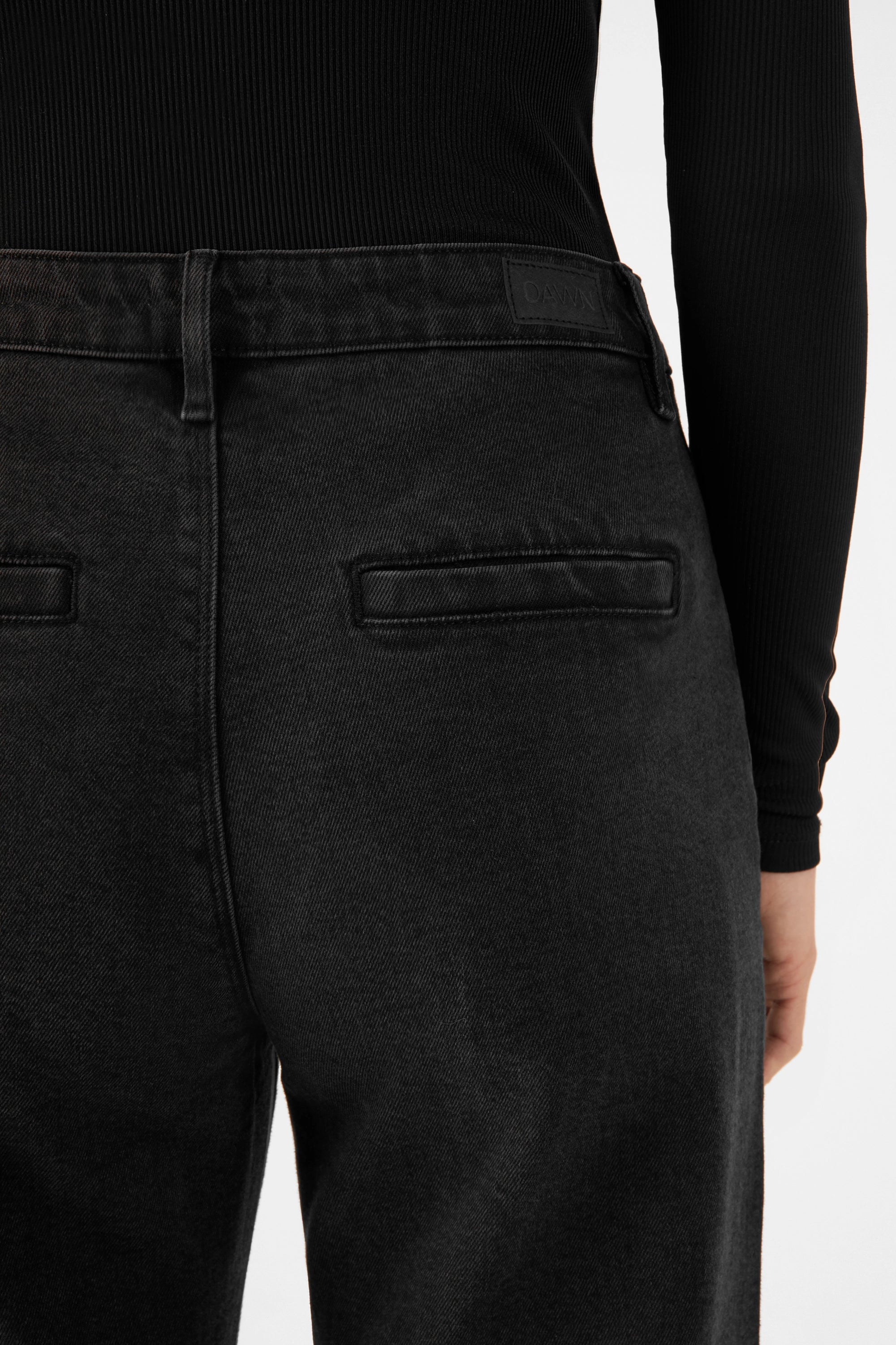 Rückansicht einer schwarzen Vintage Black GLOW Denim-Chino; mittelhohe Taille, zwei Paspeltaschen hinten, DAWN-Label am Bund.