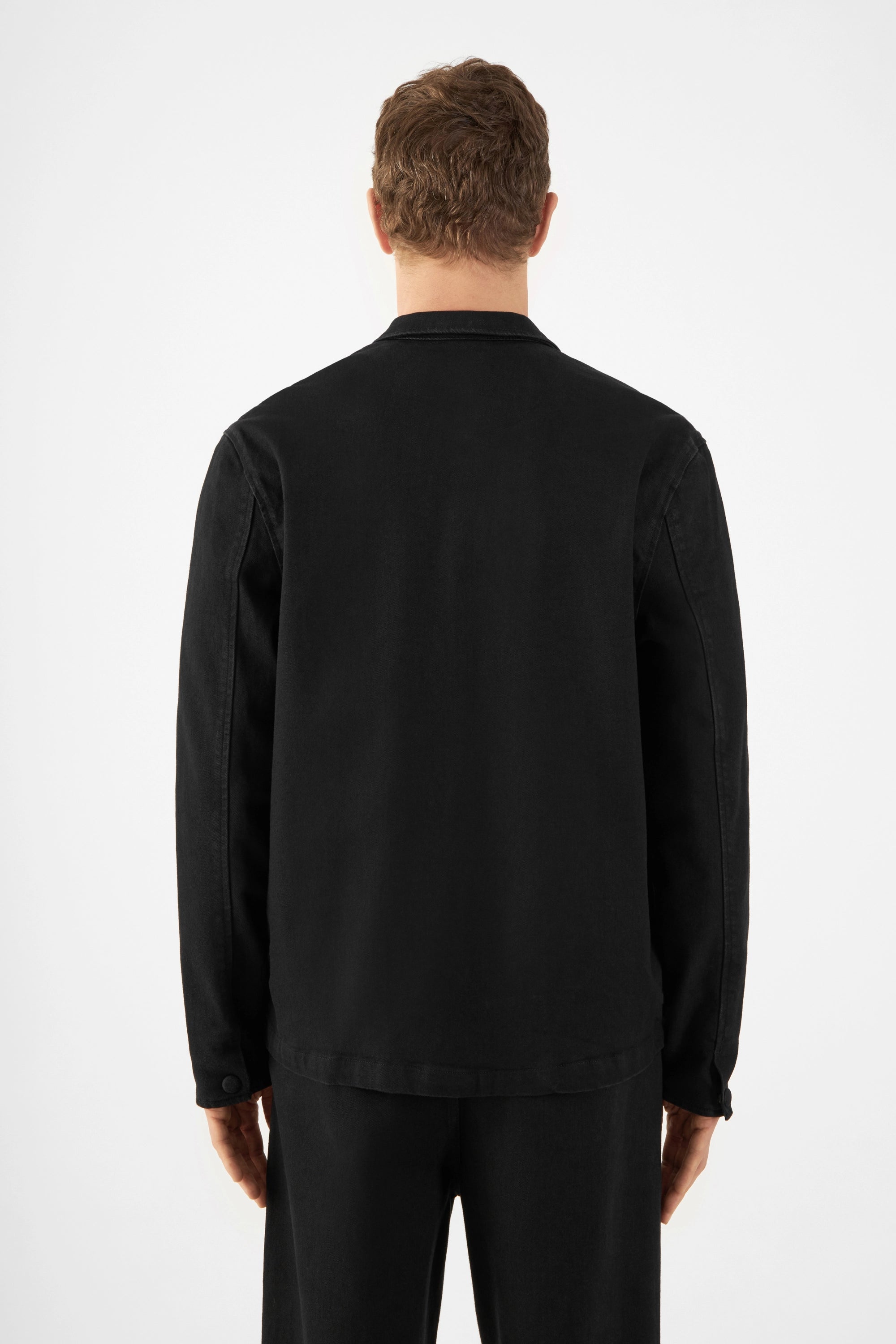 Rückansicht einer schwarzen QUIET-Herrenjacke aus Soft Denim TENCEL, locker-kastiger Schnitt, sitzt auf der Hüfte, minimalistischer Look.