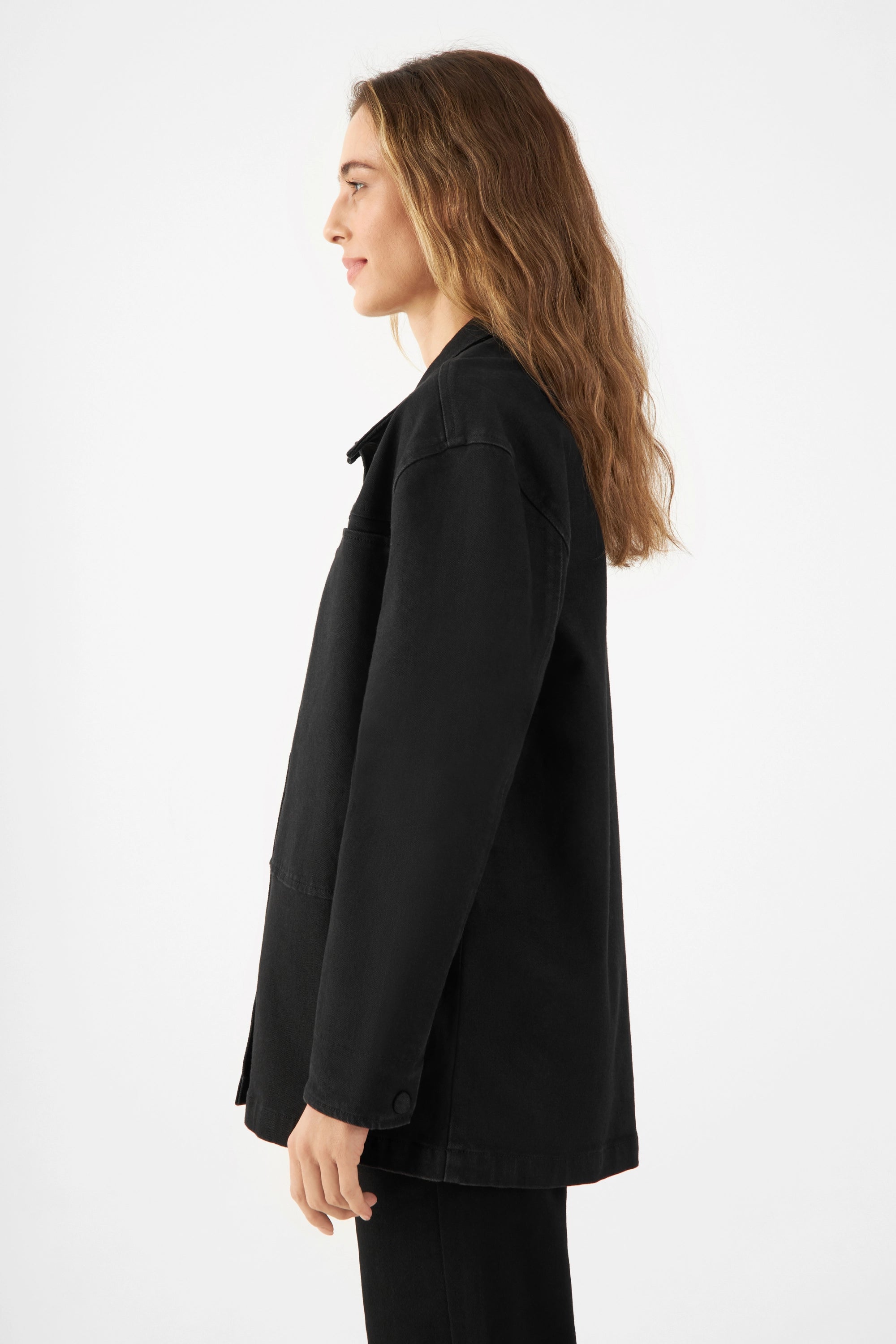 Seitenansicht einer Frau in schwarze QUIET Jacke aus Soft Denim TENCEL™, locker geschnitten, kastige Silhouette, minimalistischer Look.